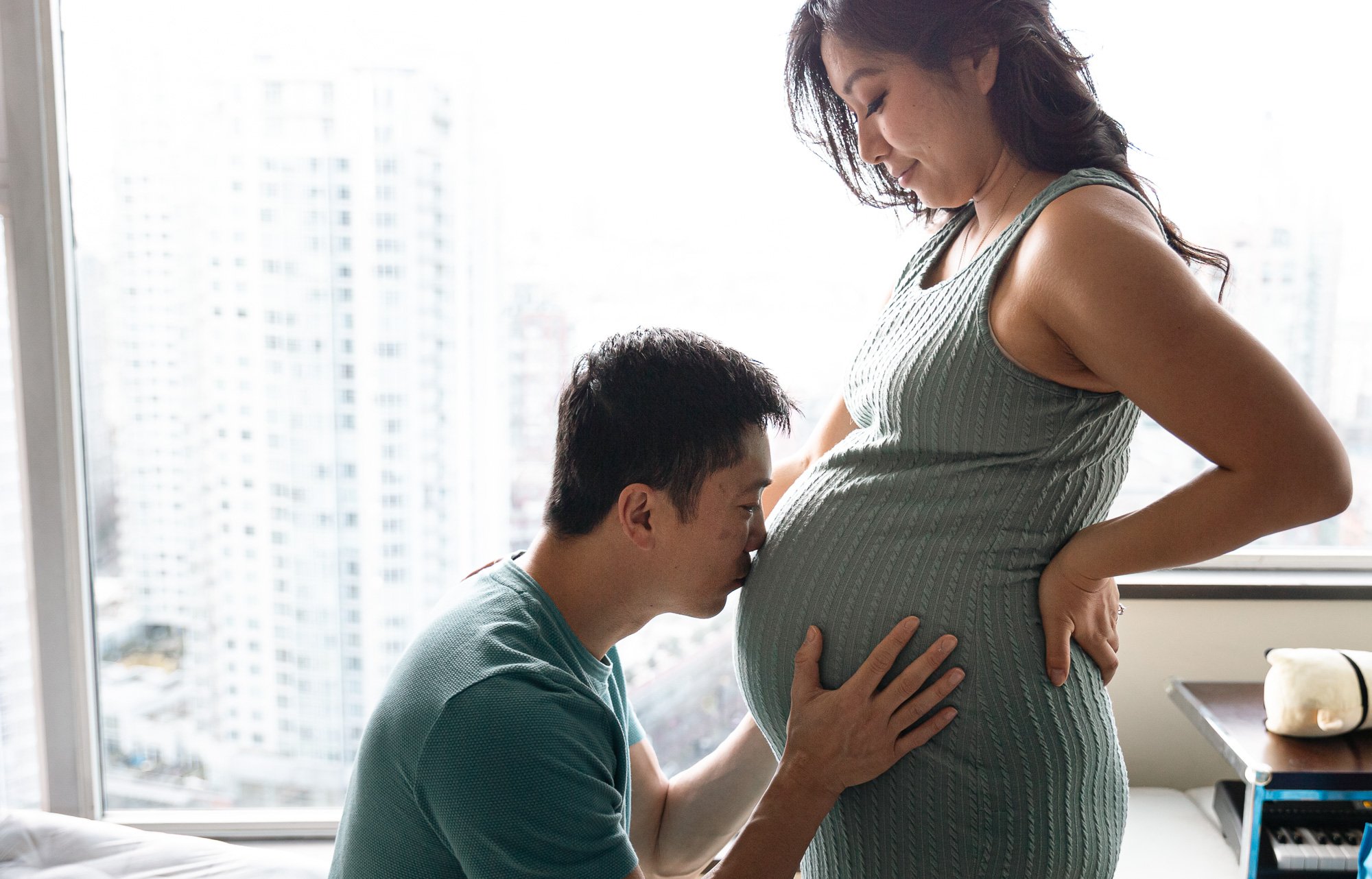 Man kissing pregnant woman on her belly in a hospital room.