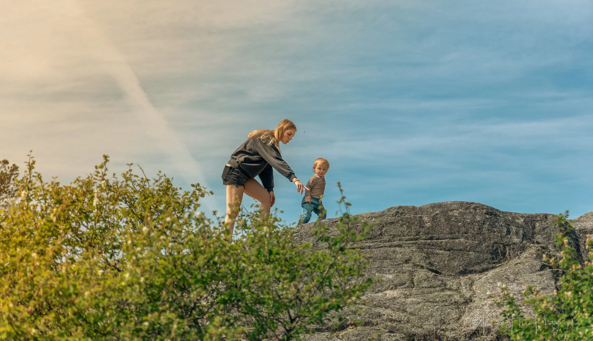 Mother reaching to help toddler daughter climb rocks at Juniper Point, West Vancouver family photo location