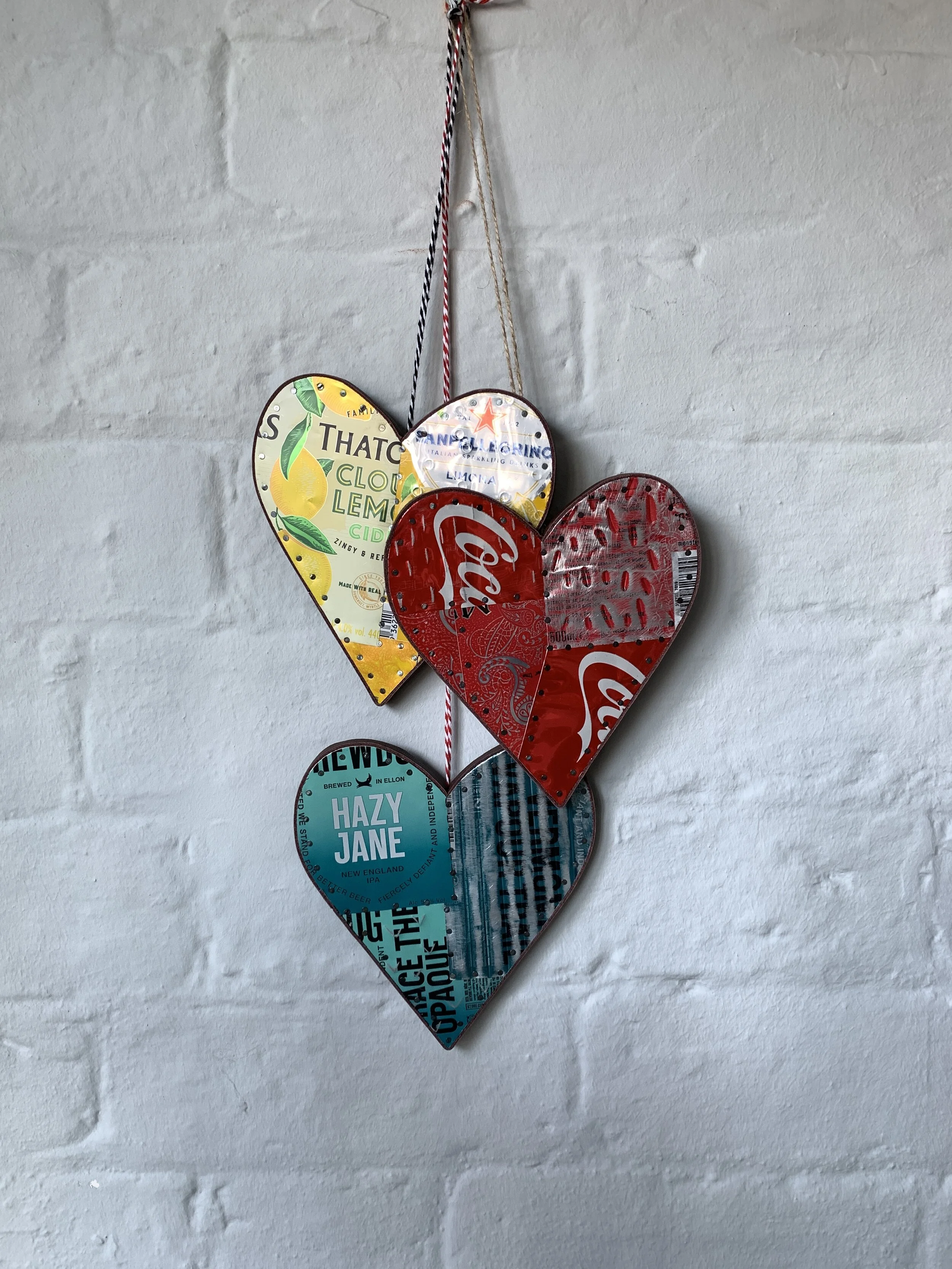 a display of Three handmade drinks can meat decorative hearts in yellow re and blue agains a white wall