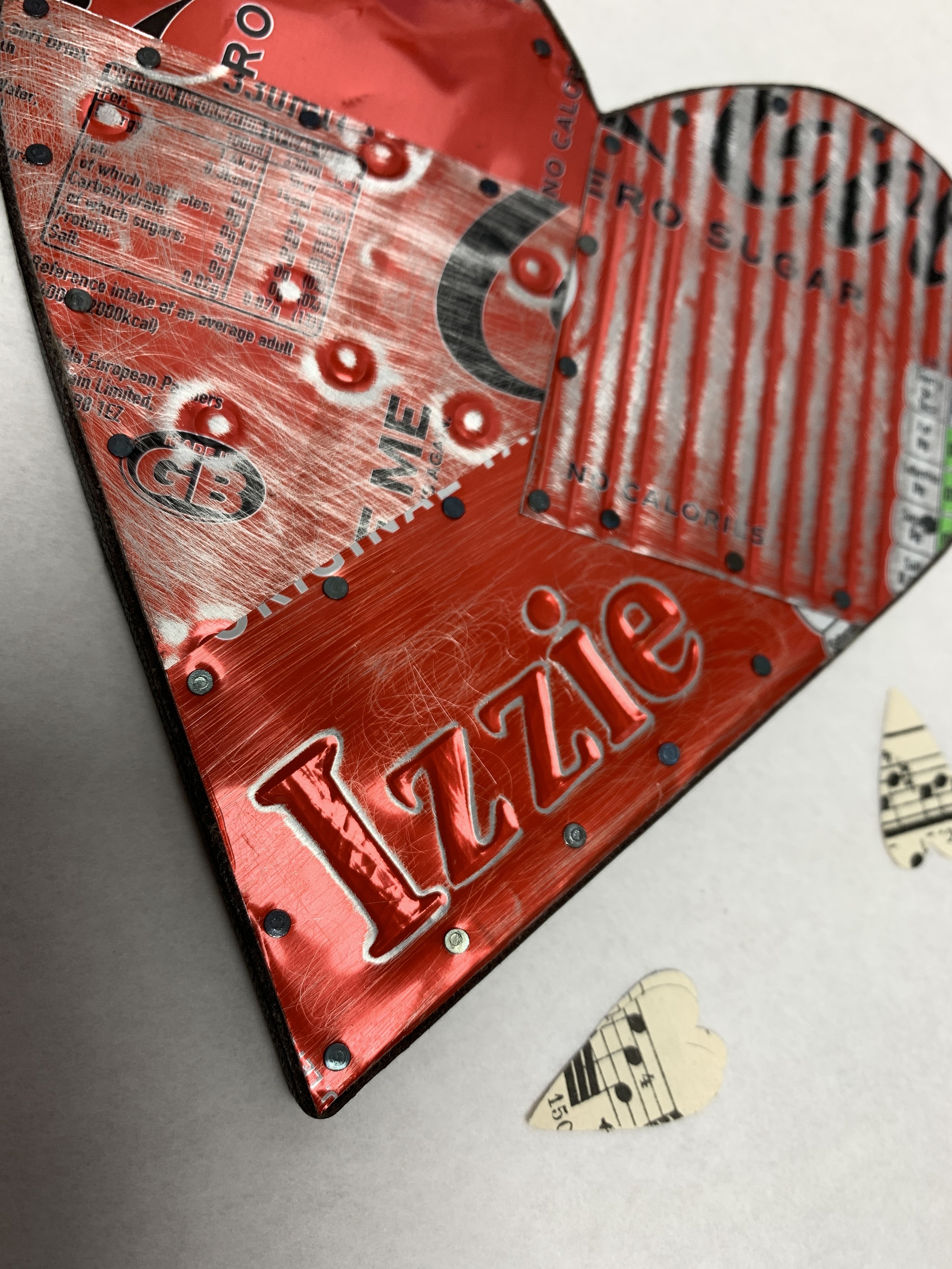 Detail of handmade red metal heart decorated with circles and stripes with the name Izzie embossed on it