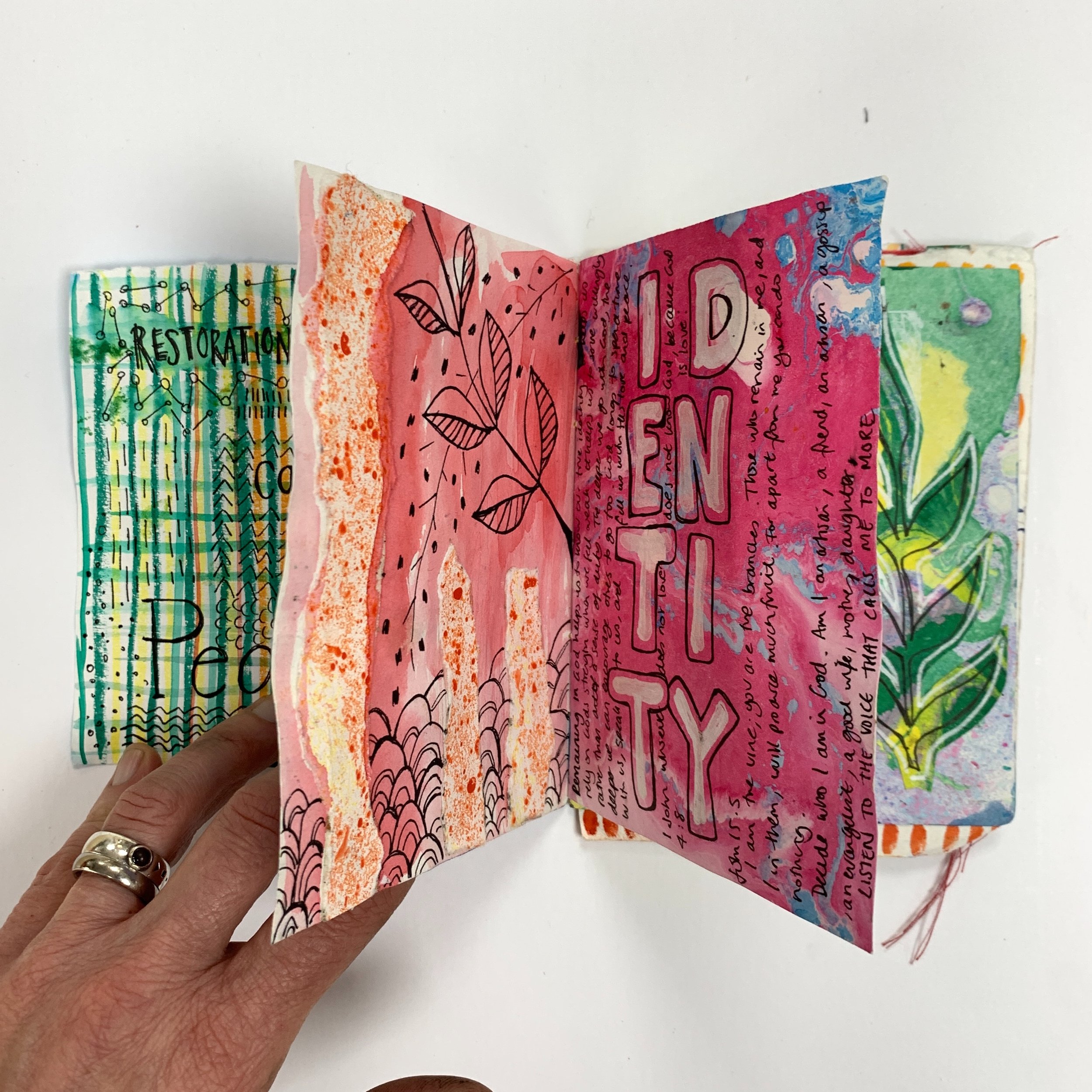 Hand made sketchbook and journal with collage text and fonts and drawing hand holding booklet open mixed media journal