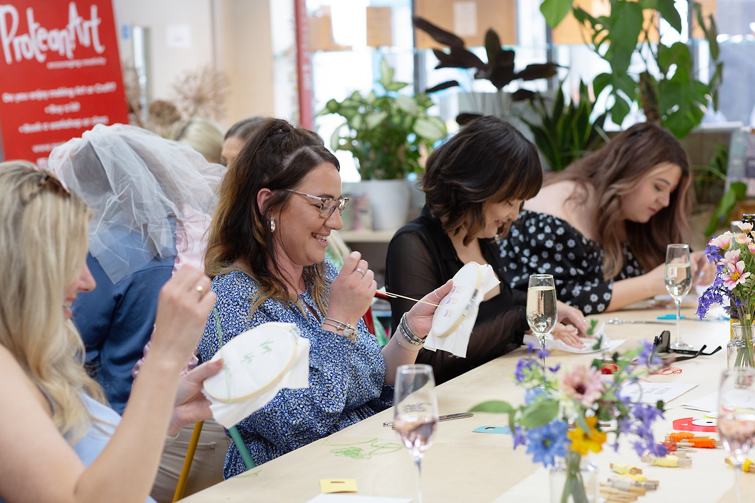 Table of happy ladies women at art party hen party stitching hanging fun flowers drinks family Proteanart