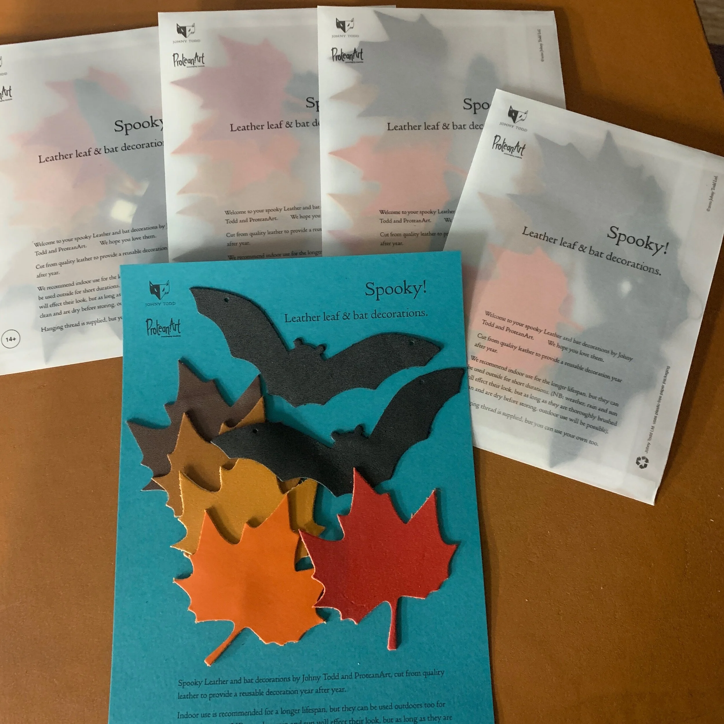 Bat and leaf shoes cut out in leather on blue card next to 4 envelopes of spooky halloween decoration packssh