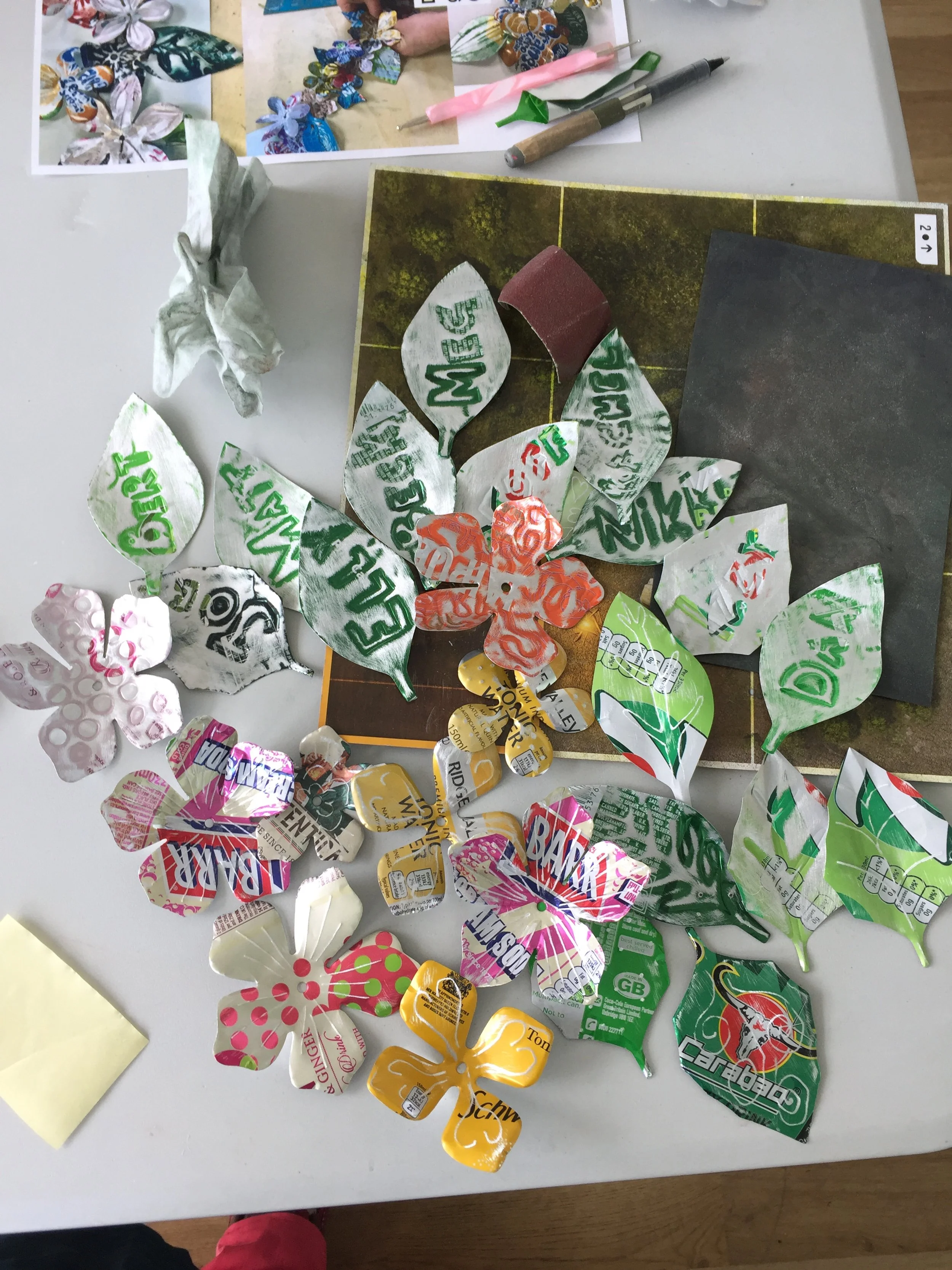 Soda can metal leaves and flower shapes on a desk with a rubber mat during an evening art class in Staffordshire