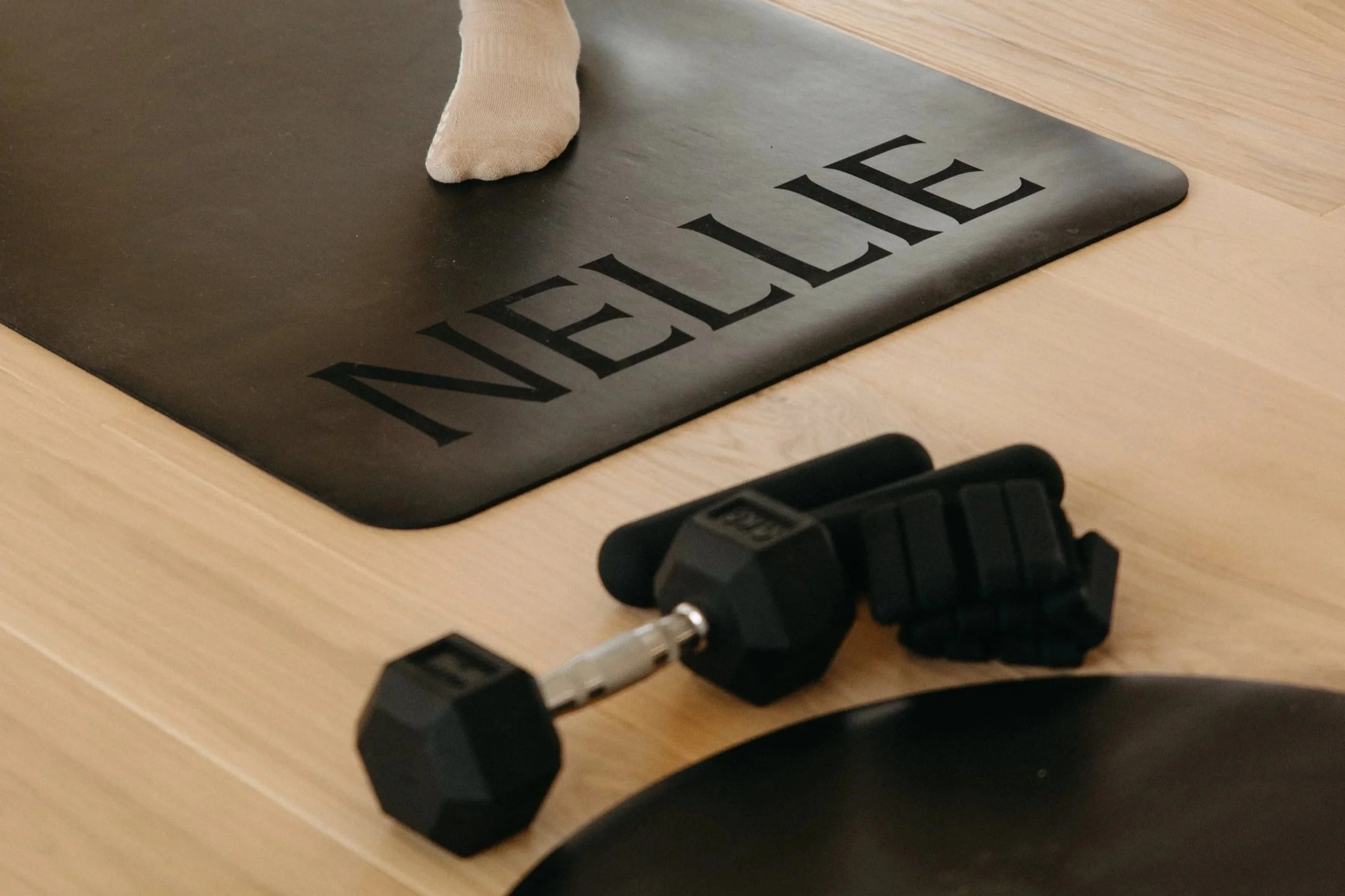 A black doormat with the word 'WELCOME' written in large black letters, a section of a beige sock, a black power strip, and a black extension cord on a light-colored wooden floor.