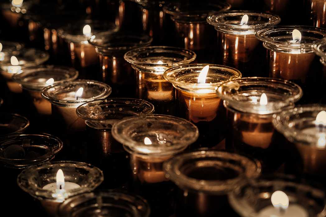 A serene, atmospheric close-up of glowing votive candles in amber glass holders. The warm golden flames flickers softly against deep shadows, creating a tranquil and cozy environment. Ideal for bringing a calming, peaceful ambiance to your home or of
