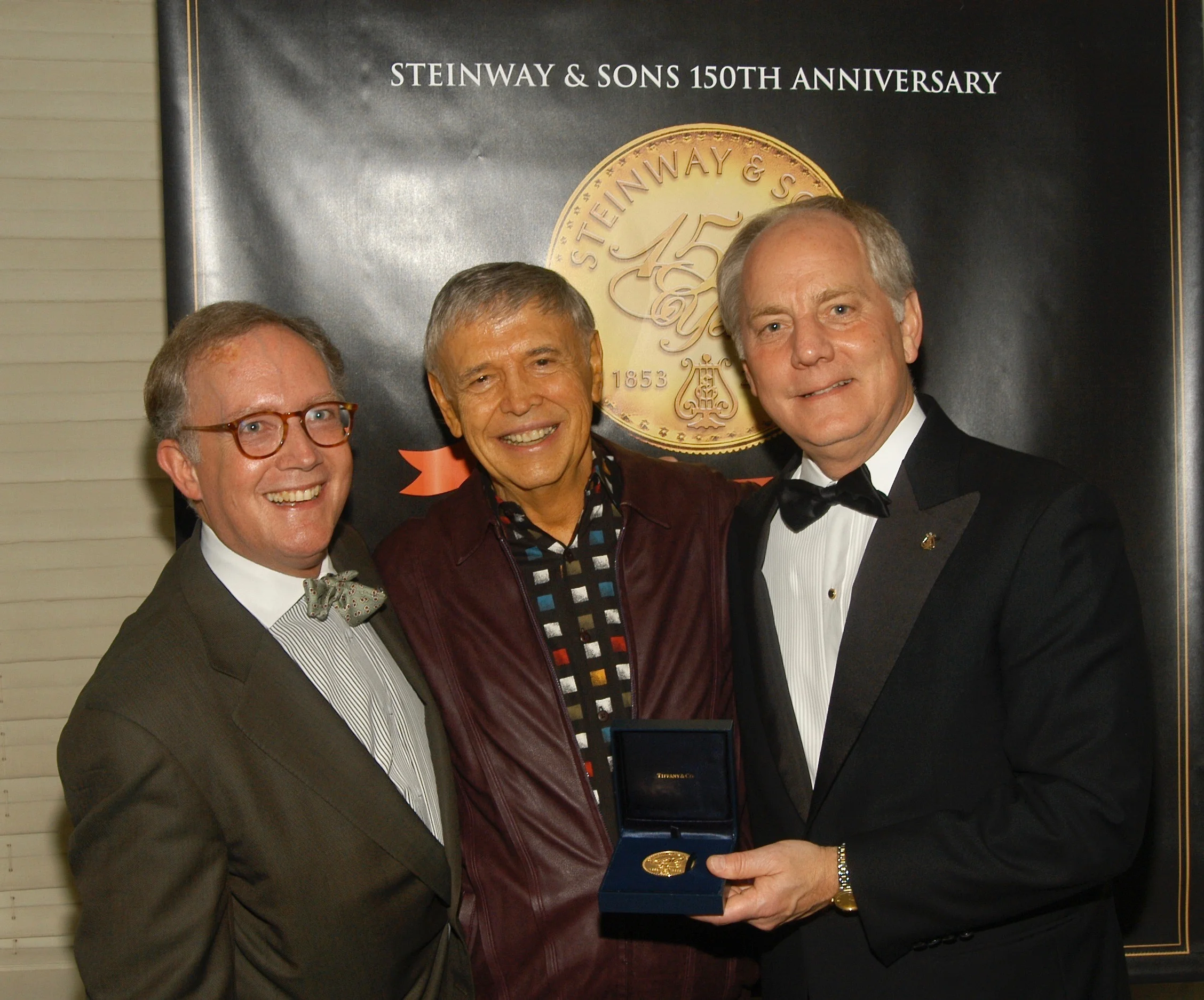 Steinway & Sons Vice President Peter Goodrich (L) and President Bruce Stevens (R) present Roger Williams a commemorative medal backstage at Steinway 's 150th anniversary celebration at Carnegie Hall 