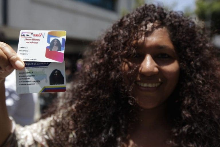 A young woman holding a Homeland Card (Carnet de la Patria), one of the economic measures to combat the economic war. Source: albaciudad.org