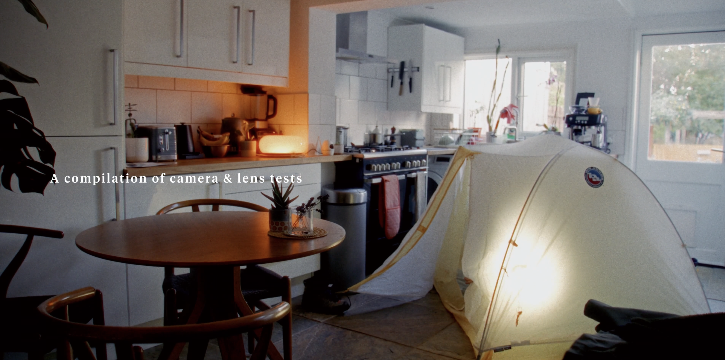 Kitchen with sunlight, a round dining table with two chairs, a tent partially set up in the foreground, and various kitchen appliances and utensils on the counter.