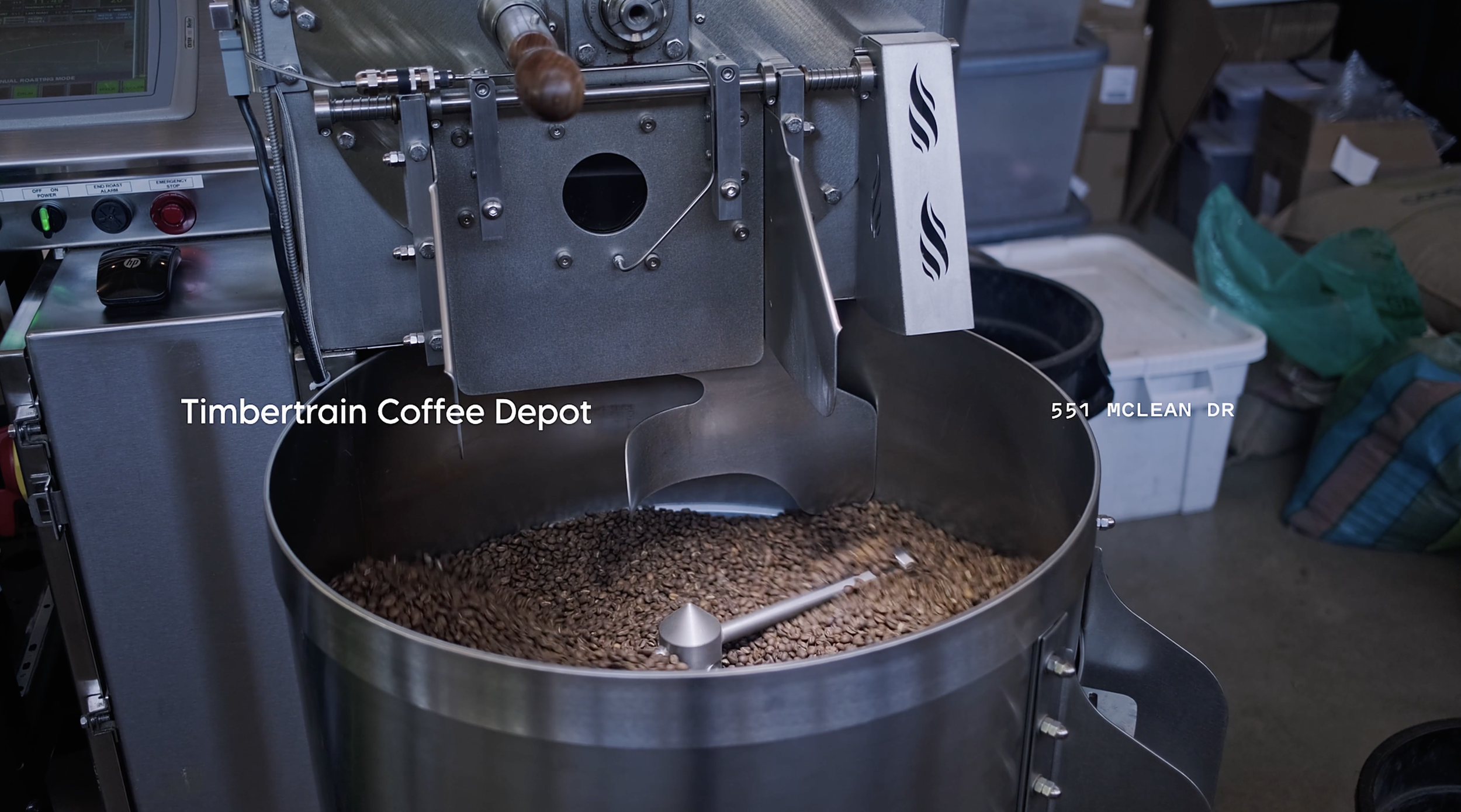 Commercial coffee roasting machine with roasted coffee beans inside, in a coffee shop or roastery environment.
