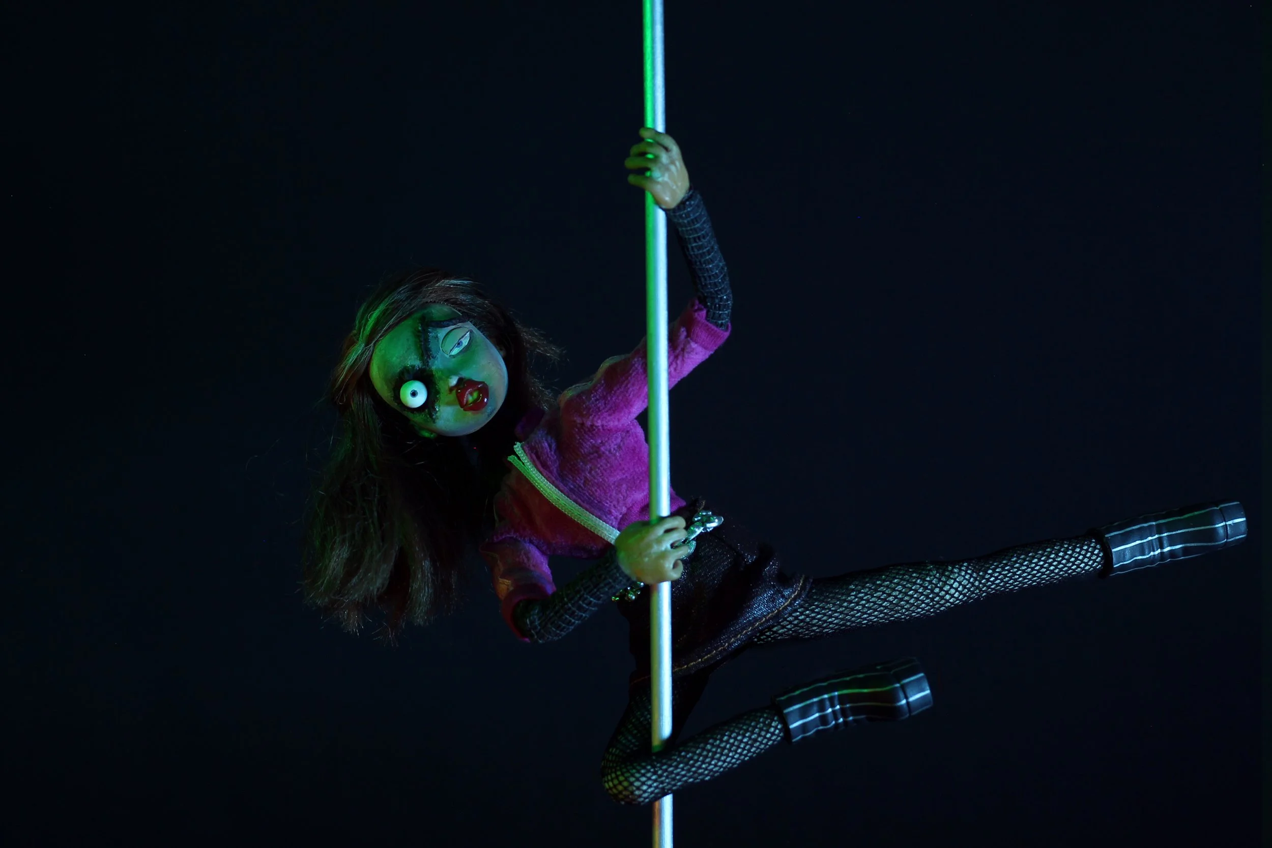 An animated, one-eyed doll dressed in a pink coat, black dress and fishnet tights is poledancing.