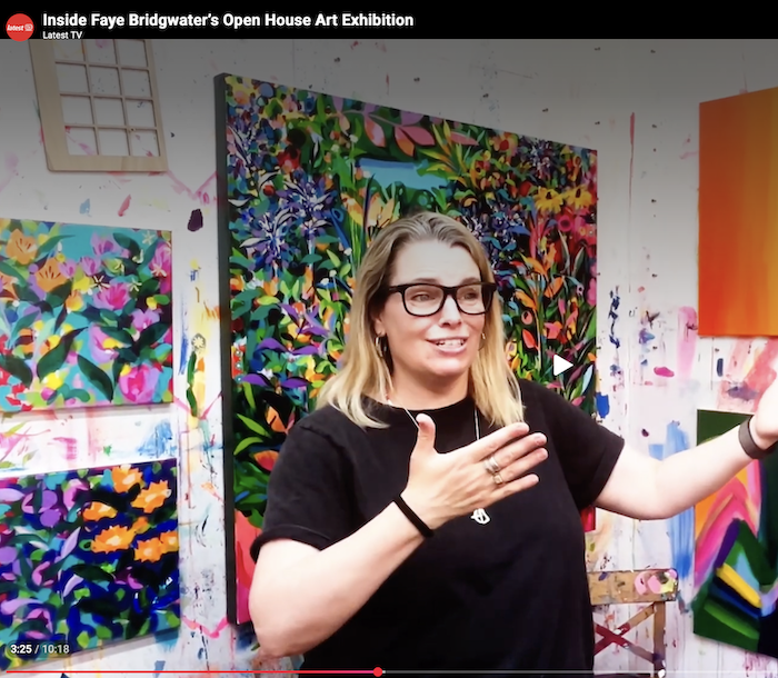 Faye Bridgwater being interviewed in her studio, with her colourful landscape and floral paintings