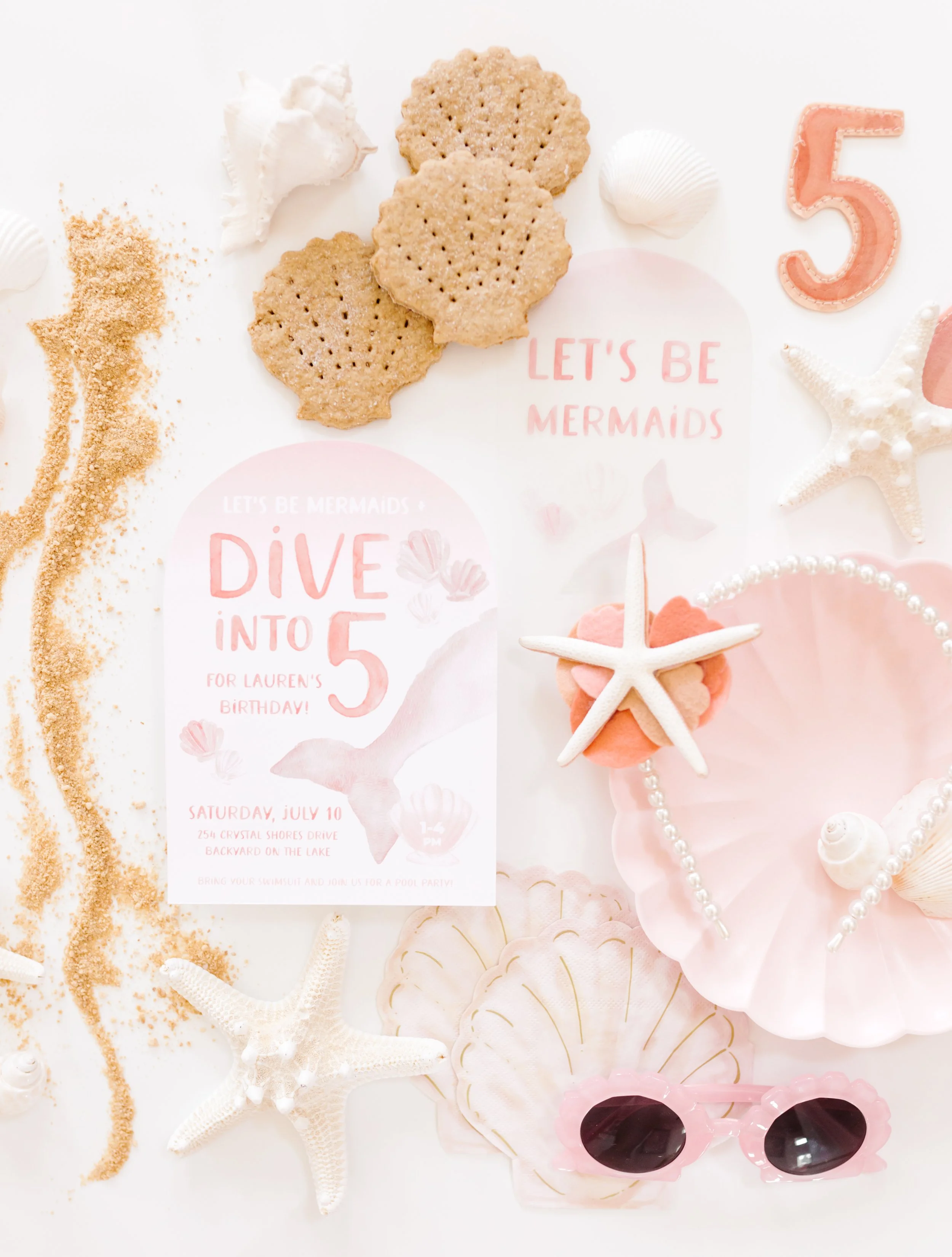 Sea-themed birthday party decorations including seashells, starfish, mermaid tail party favor, pink sunglasses, starfish, pink and peach cookies, and an invitation for a mermaid-themed birthday party.