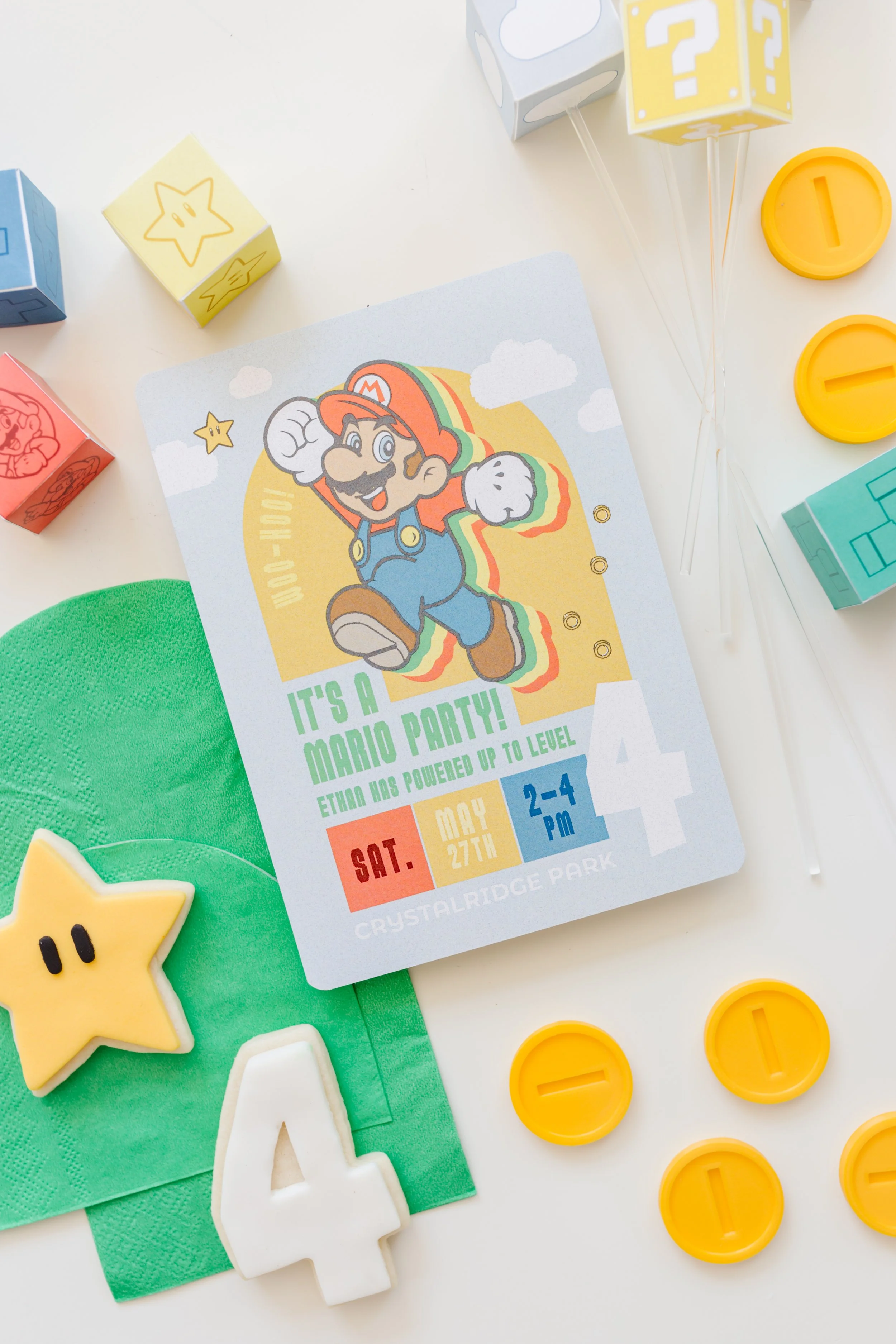 Invitation for a Mario-themed birthday party with decorations including a colorful card featuring Mario, game themed candies, and coins.