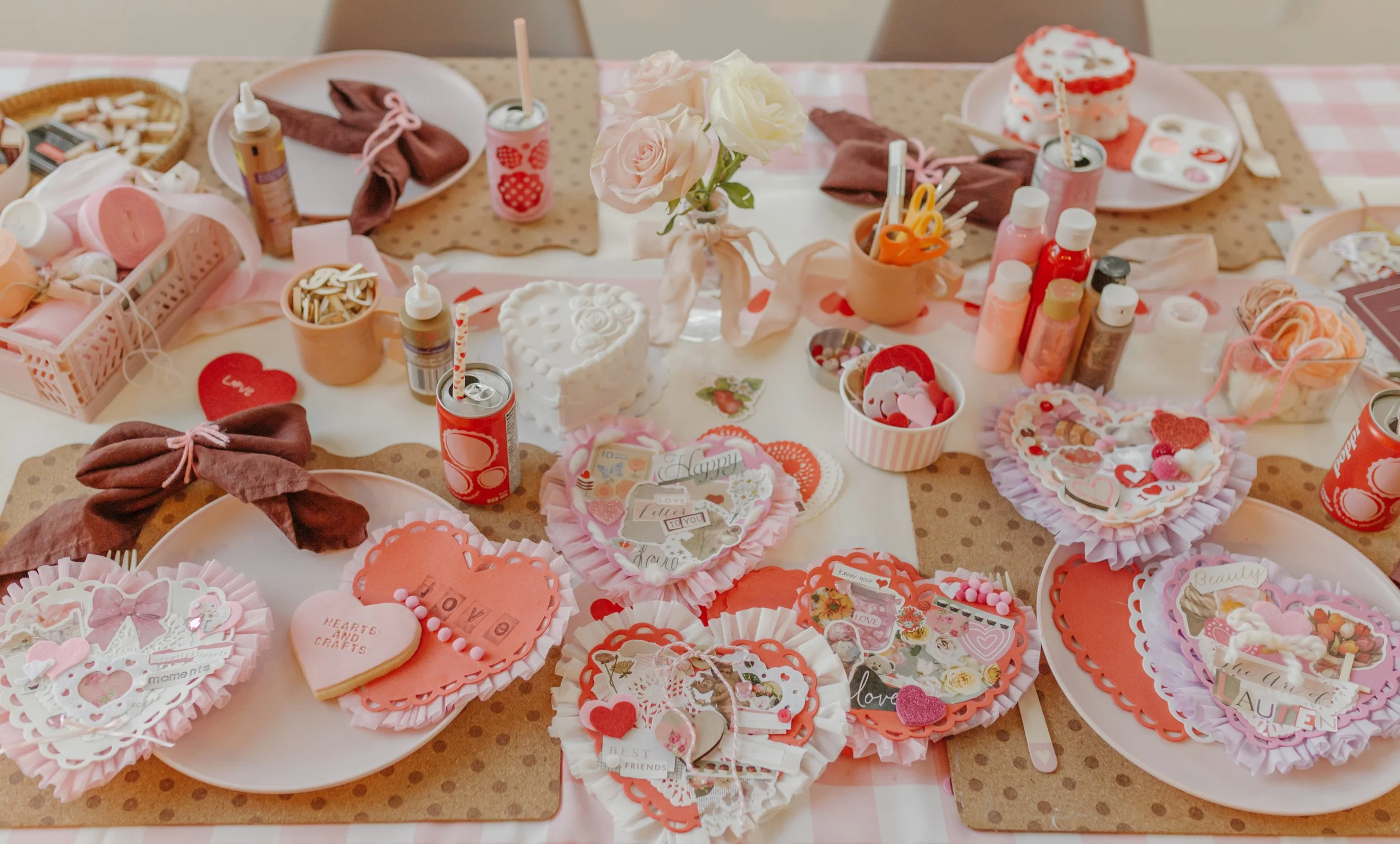festive valentine's day table set up for an art project making heart-shaped collages - with streamers, paper doilies, stickers and yarn.