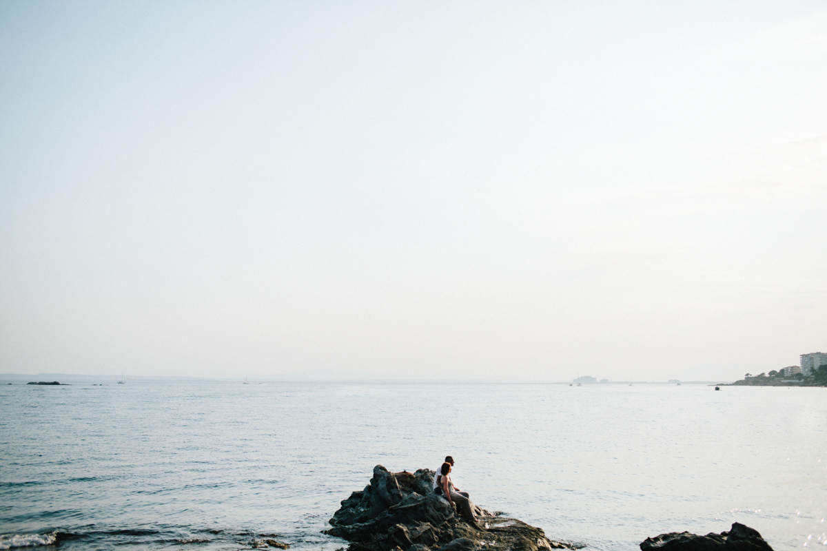 Sea landscape with a rock and a couple sitting on it.