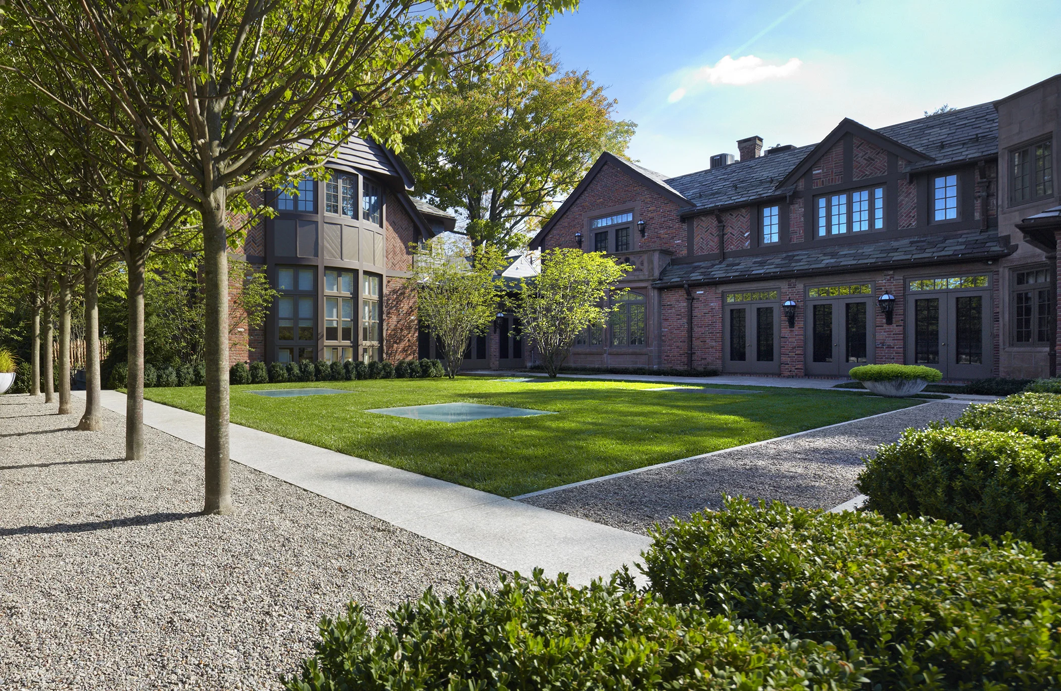 This property occupies a corner site in a historic neighborhood of Newton. As avid art collectors, the Owners envisioned a museum addition below the rear of the property that left a large part of the landscape on structure. This gallery space was designed to integrate fully into the site, with flush skylights that puncture a lawn panel for entertaining, and a glass head house as a focal point of the garden, that also allows significant pieces of sculpture to be brought into the gallery below. A series of outdoor spaces comprised of gravel, granite and lawn become a neutral framework for an expanding sculpture collection. Pleached lindens punctuate the installation at the glass head house, while espalier oak trees screen the street beyond, and form the backdrop for landscape sculpture. A long linear garden of hedges and witchhazel establish a repetitive rhythm that connects the rear gardens to the front of house, where the planting forms a pattern language. From the street side, the site design remains restrained and elegant, with weathered bluestone, minimal lawn and groundcover, responding to the historic context of the surrounding neighborhood. Photography Charles Mayer
