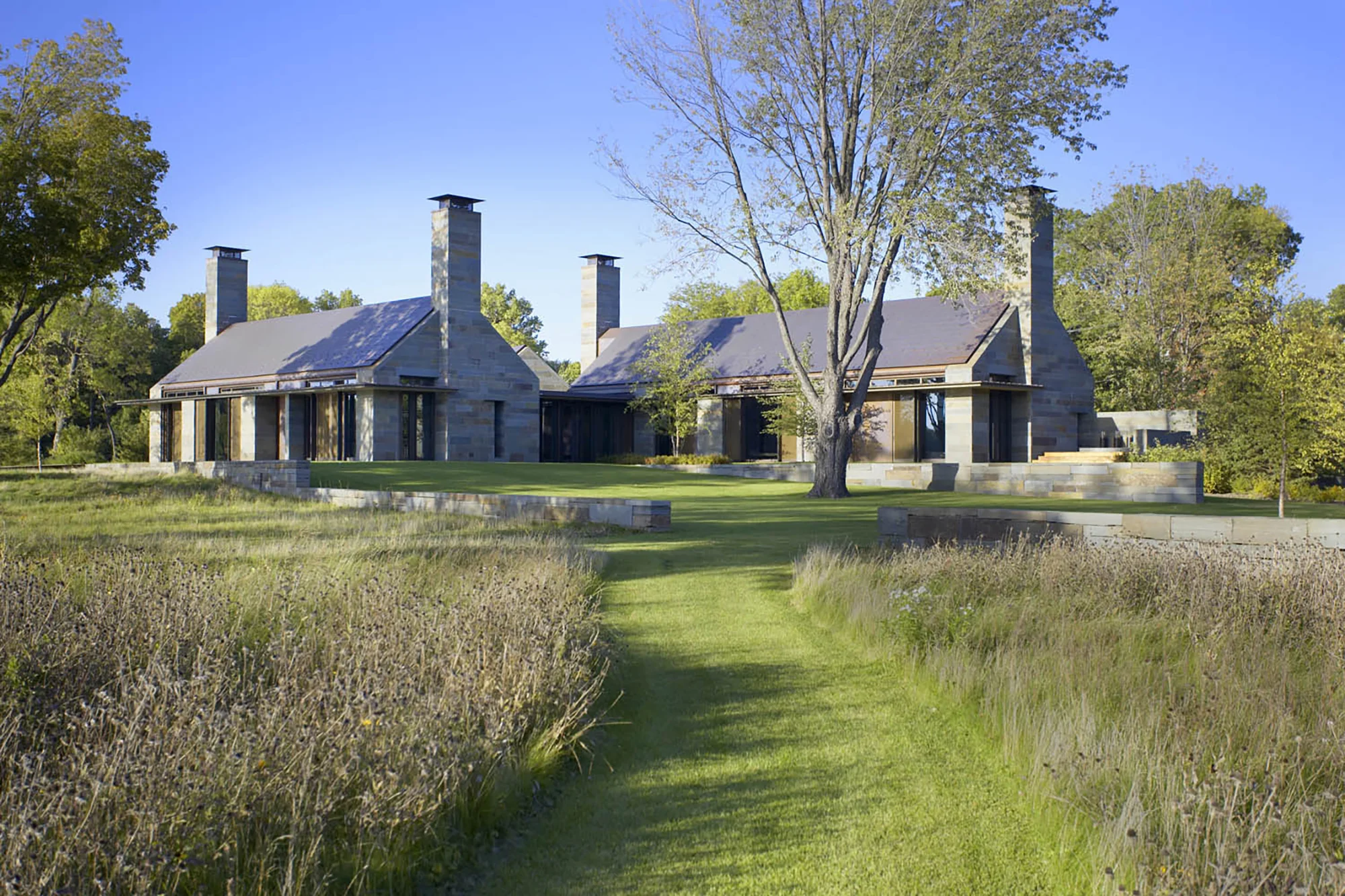This residence on the shore of Lake Minnetonka consists of segmented living quarters connected by social spaces and a central terrace. The building is oriented to take advantage of views to the north and southwest. A series of stone retaining walls create elevated platforms for the building, central terrace, and private terraces. The terraces and retaining walls are extensions of the interior rooms and walls, and extend the building out into the landscape. The long site walls required to raise the house above the floodplain allow gently graded slopes to blend with the lakeshore topography. Vernacular wood docks extend from the house to the water, and beyond to a trail system. Native wetland and transitional upland plant communities respect the lakeshore ecology, and site patterns reflect historic logging and farming geometries from the region. Collaborators Olson Kundig Allen Architects Photography Karen Melvin STIMSON