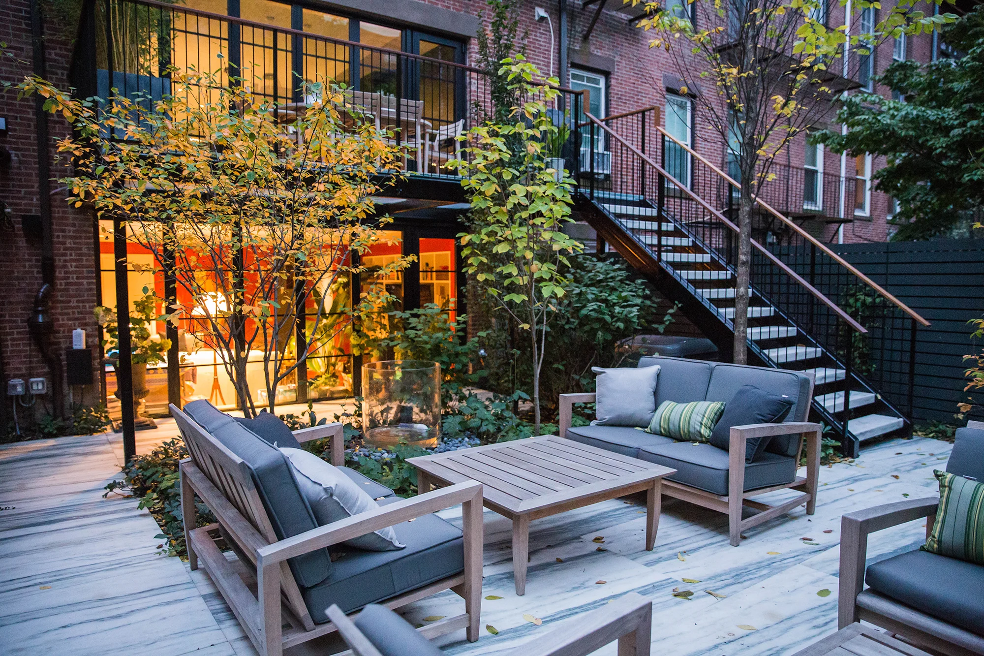 This courtyard garden in the South End of Boston provides an immersive sanctuary that extends the intimacy and materiality of the interior living spaces outdoors. A translucent glass balcony meets the main level living spaces and provides an area for outdoor dining while allowing daylight through to the lower level living spaces and terrace beneath. Marble steps connect the upper balcony with a terrace at the lower level of the same material. A cedar slat shadow box garden fence with integral lighting encloses a garden of rich textures and seasonal interest. Photography Ngoc Doan