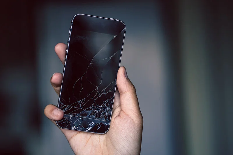 A hand holding a smart phone with a cracked screen in need of phone screen repair in Philadelphia, PA