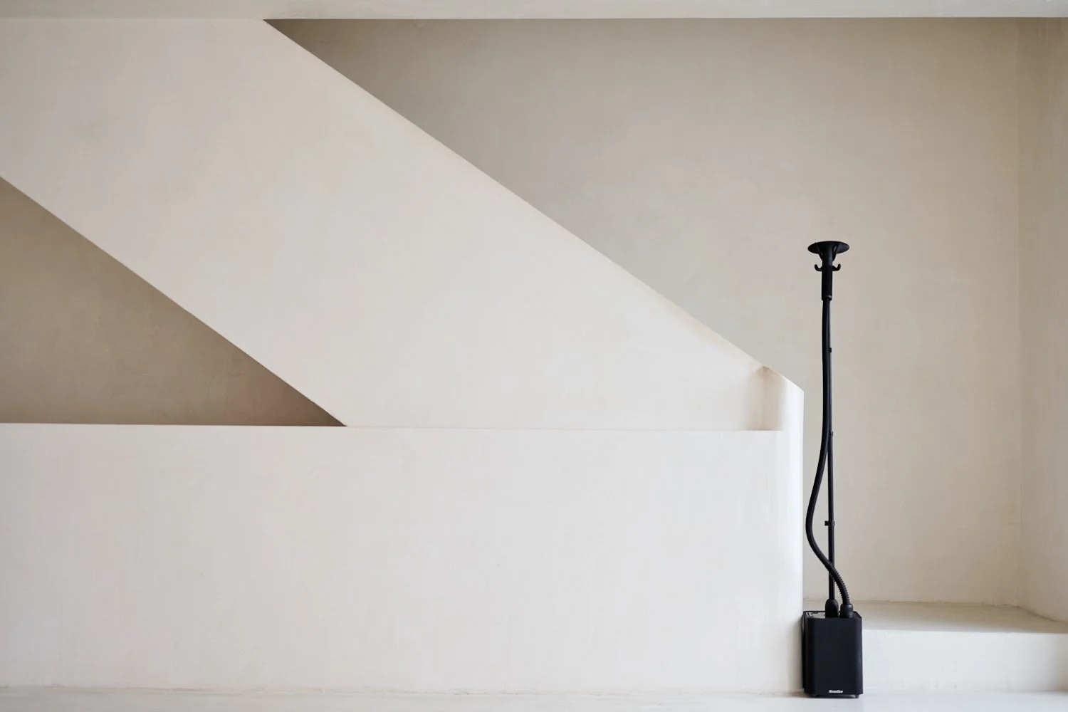 Minimalist interior with a modern black floor lamp and geometric white architectural elements against a neutral wall.