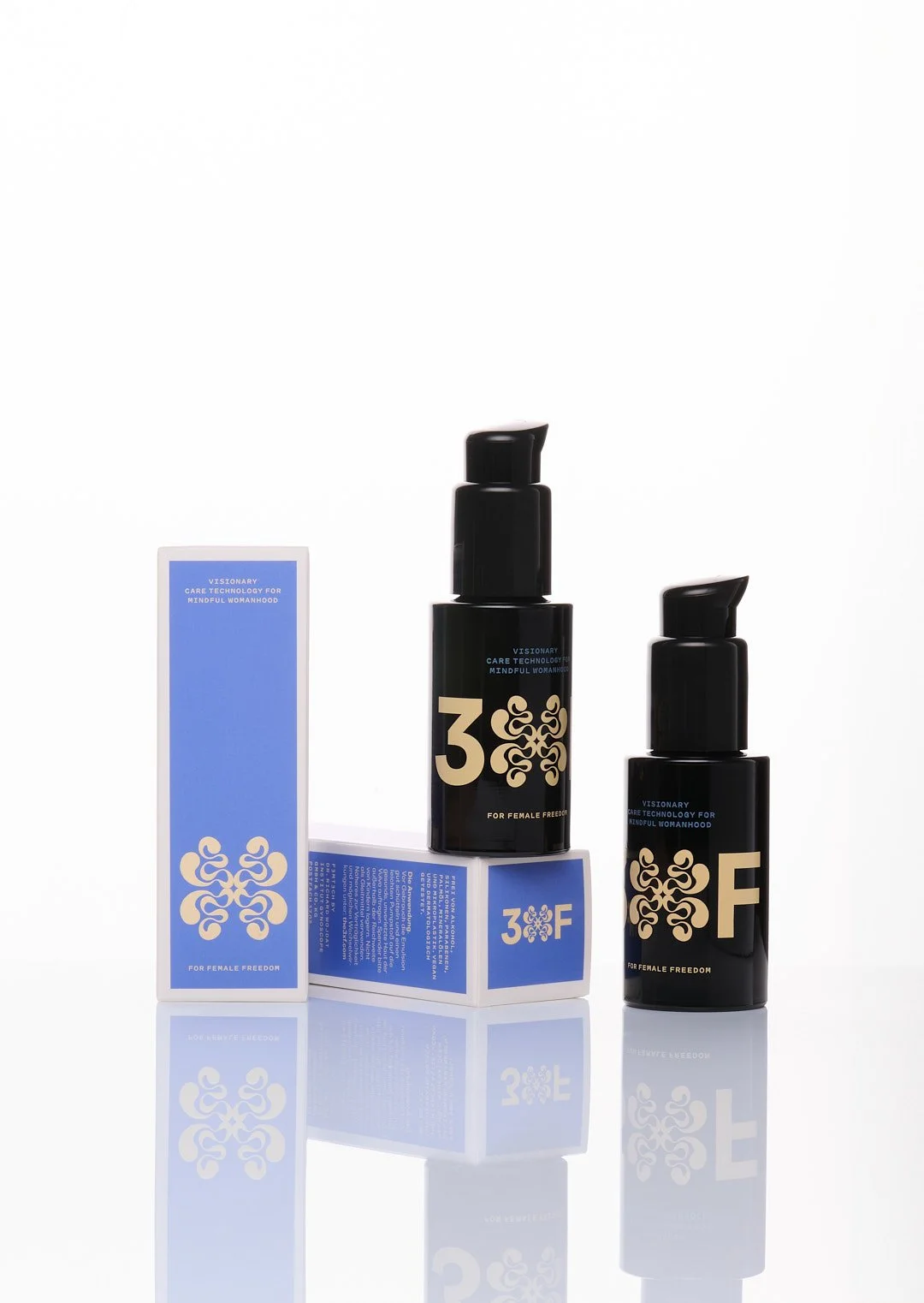 Two black bottles with pump dispensers and a blue box with white and light gold labels and text, arranged on a reflective white surface.