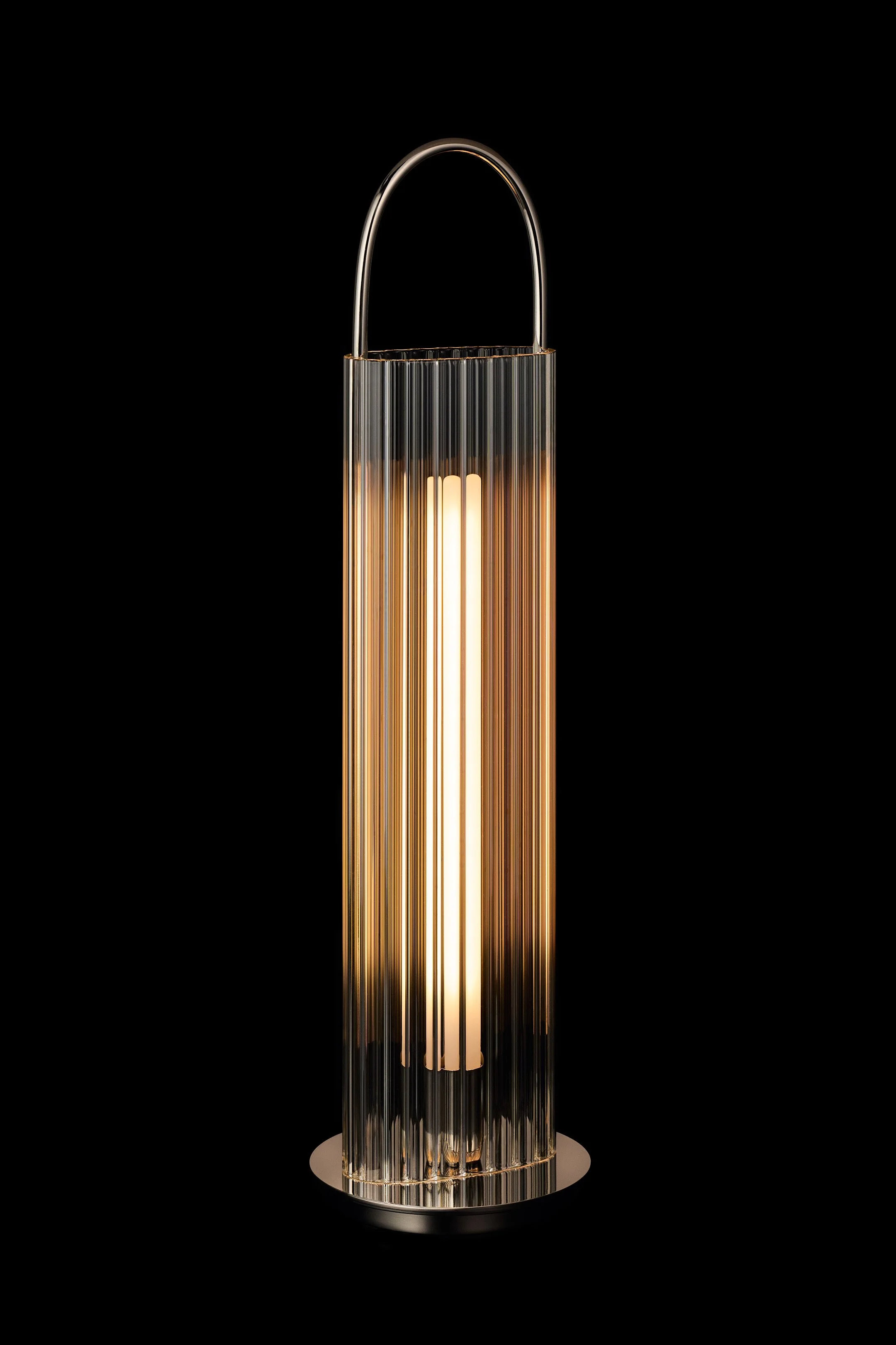 A tall, cylindrical floor lamp with vertical glass panels and a polished metallic top handle, emitting a warm glow on a dark background.