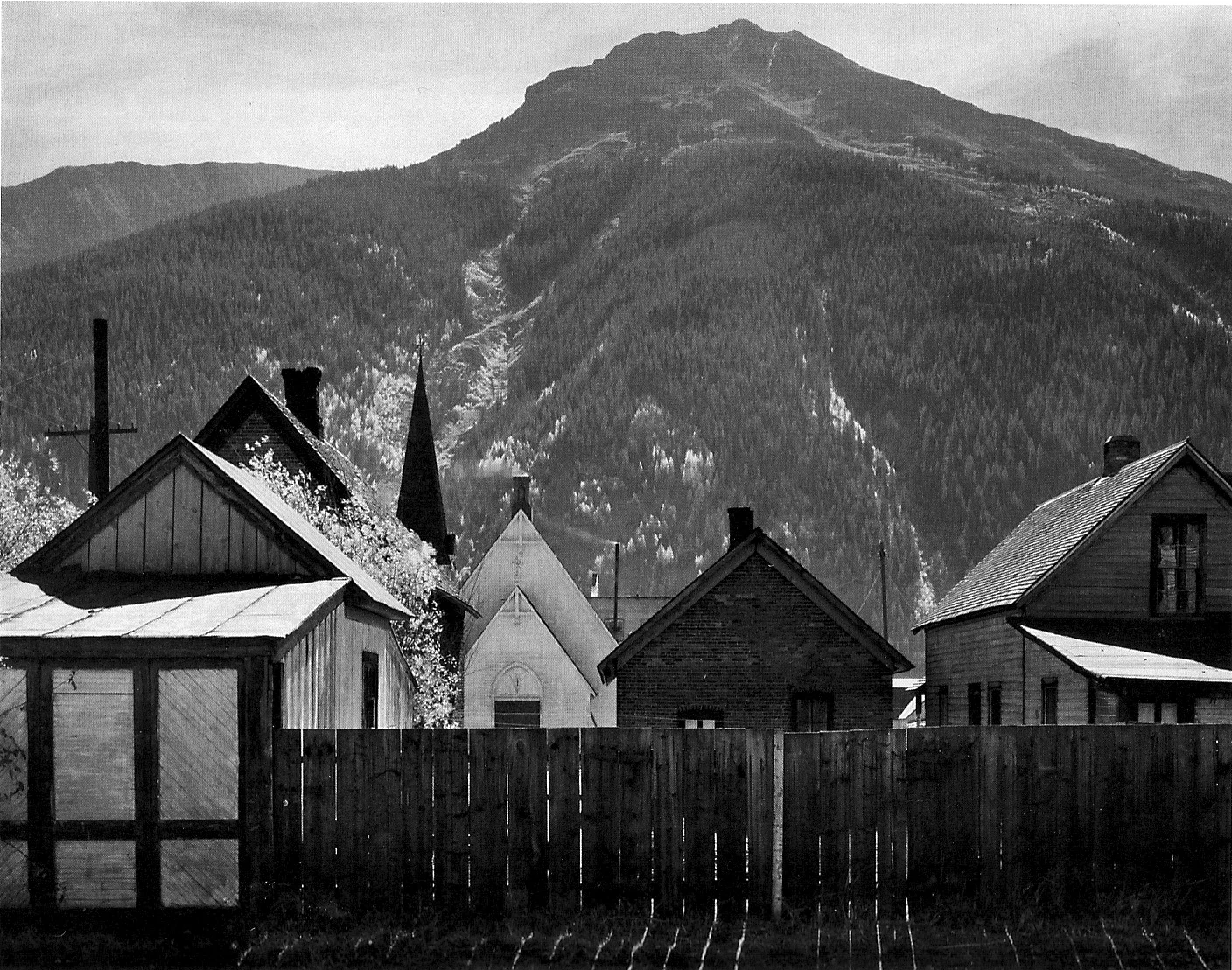 fence in front of buildings and church, behind that a tall mountain