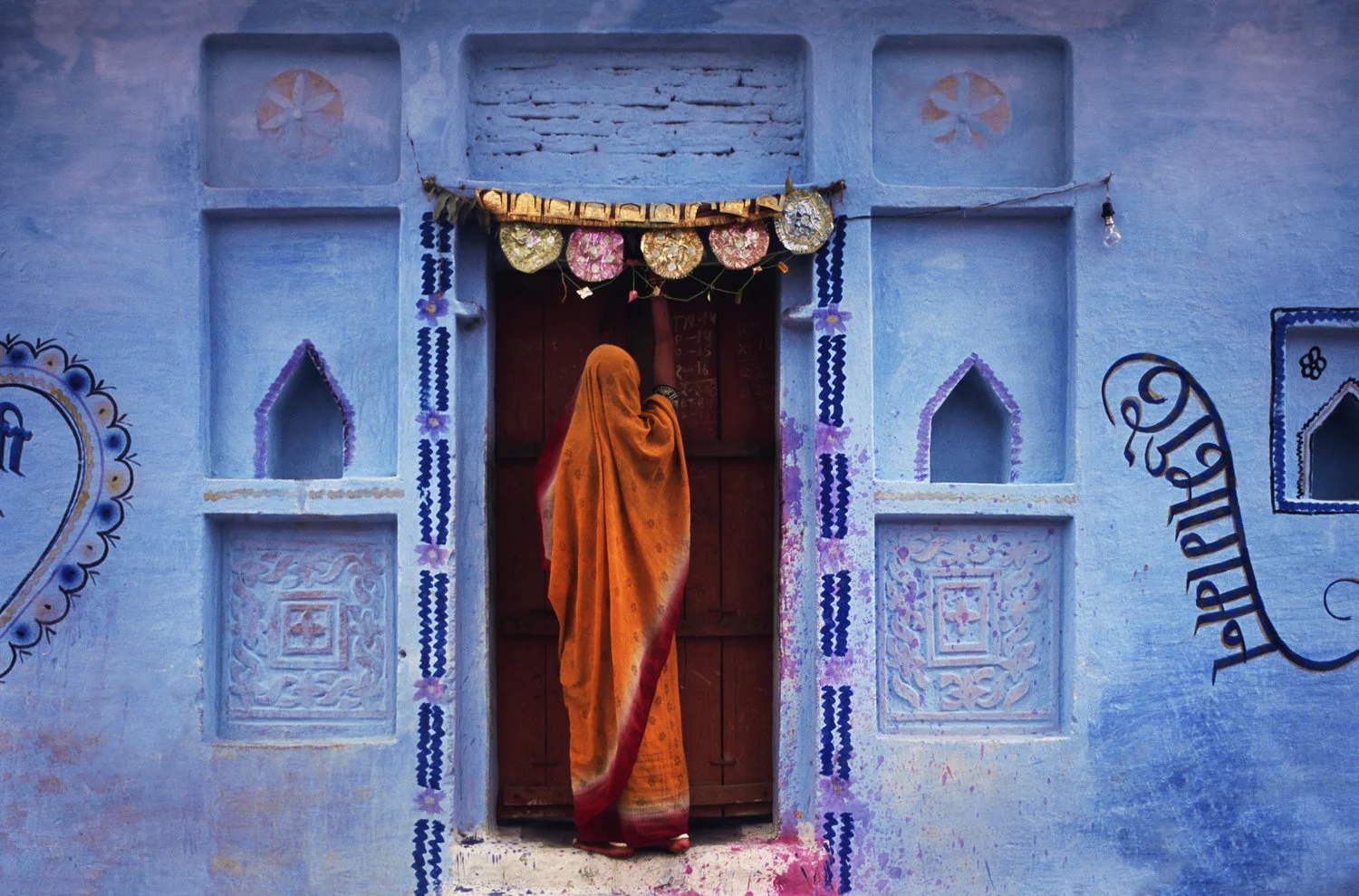 light blue building girl in orange sari entering