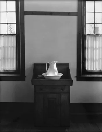 Washtub and water jug om table between windows