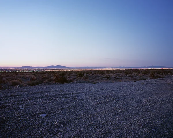 dawn looking over gravel to desert with city lights and mountains horizon