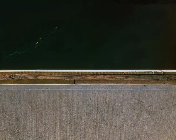 green still water bisected by dock cement wood edge