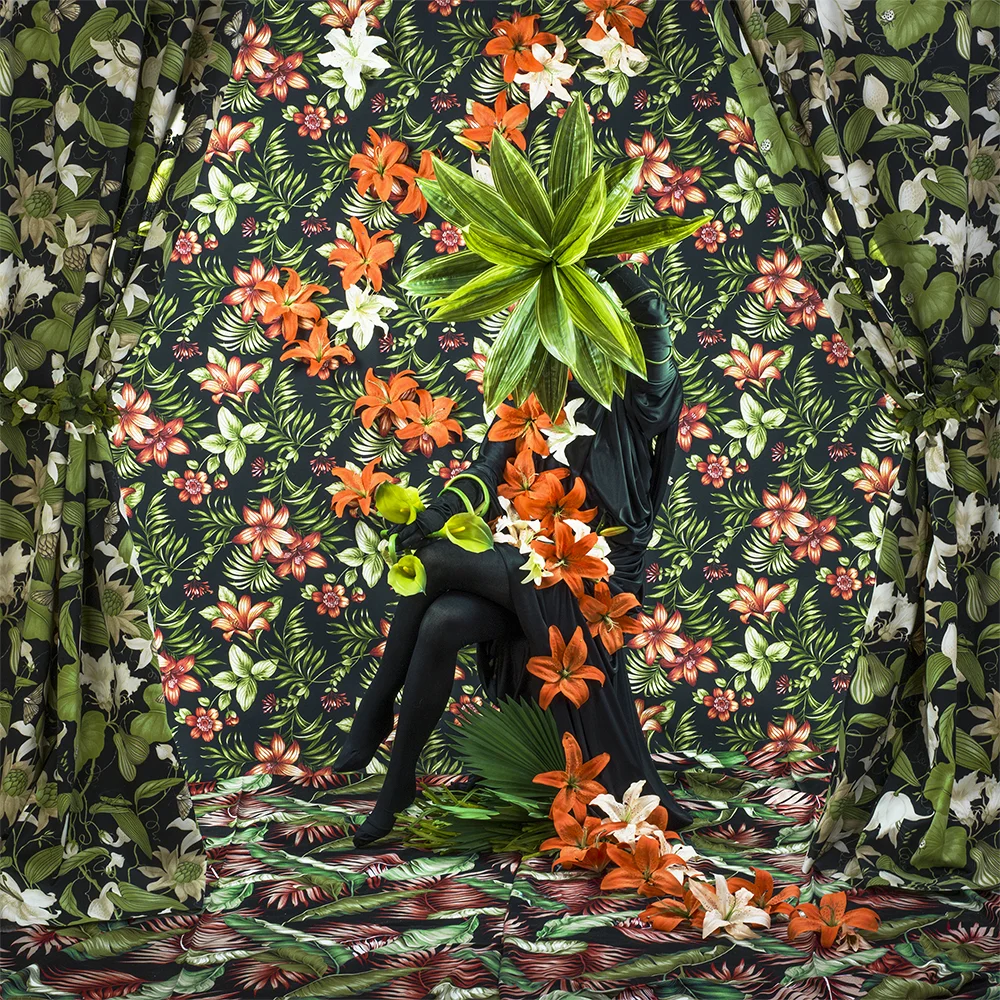 woman surrounded by lilies and lily wallpaper with leaves obscurring face