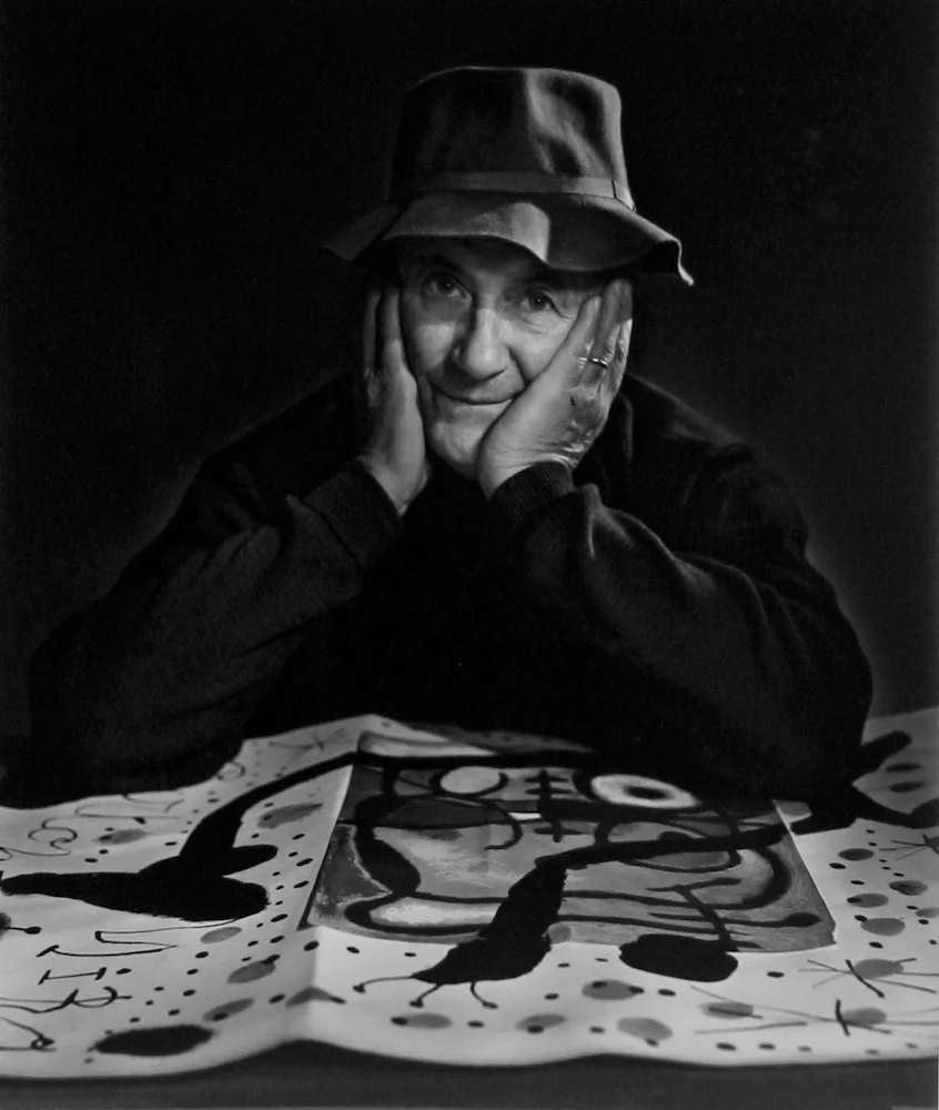 Joan Miró poses with art on table