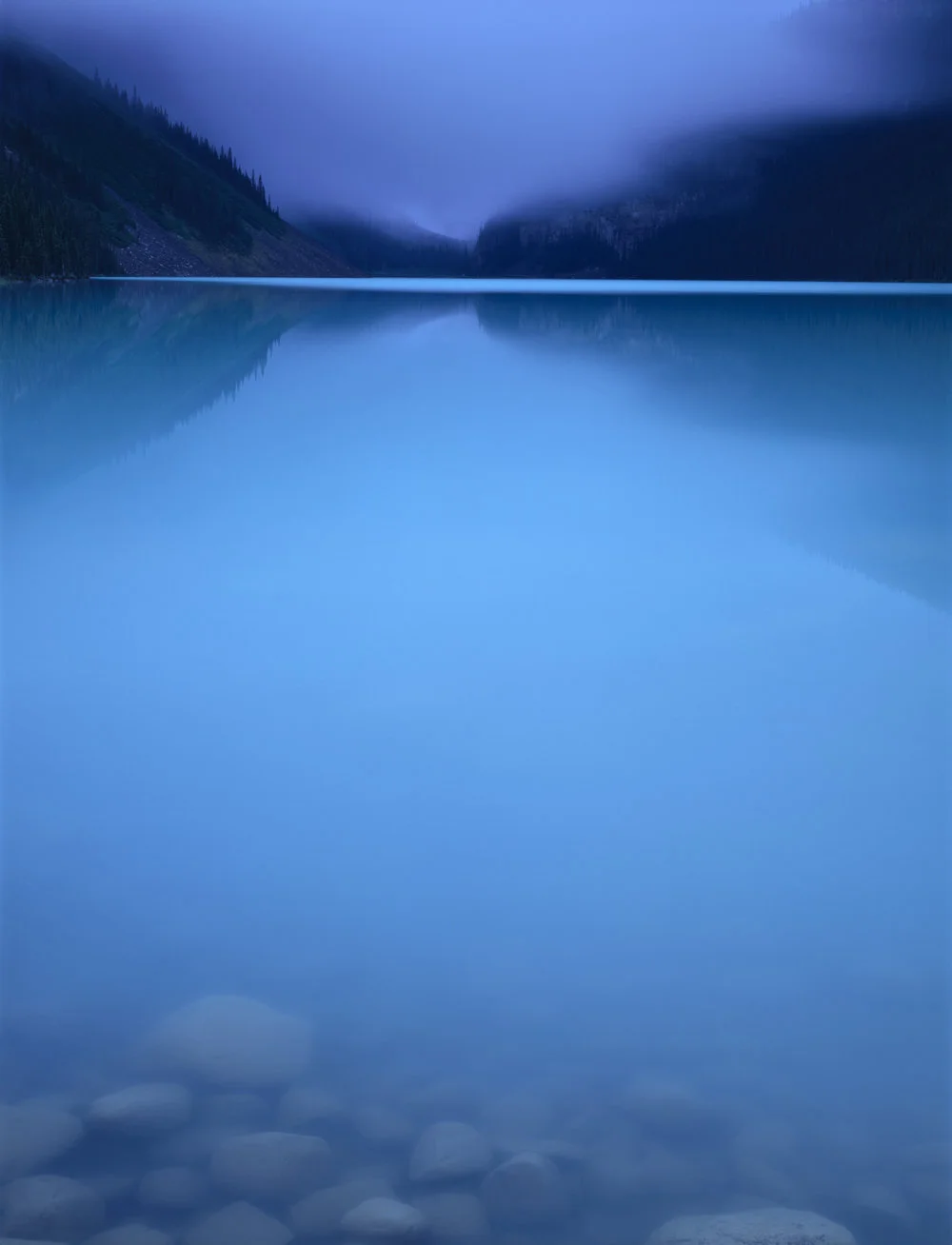 cobalt blue lake with low mist and mountains on horizon