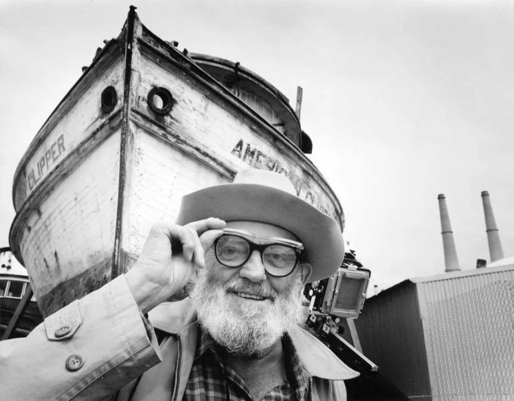 man tipping hat smiling in front of boat