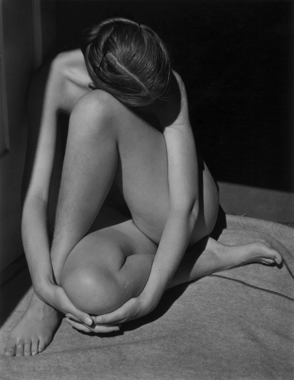 Nude woman with arms and head tucked sitting