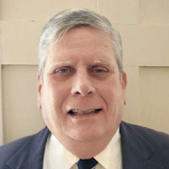 Dean Davis in a grey suit with a beige wall in the background.