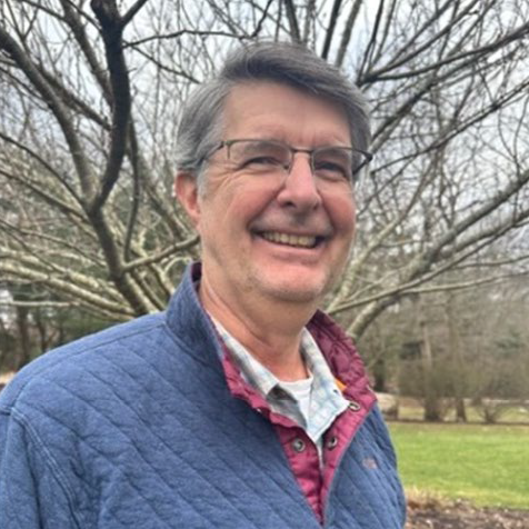 Jim Taylor standing ourside in front of a tree with a blue and maroon jacket.