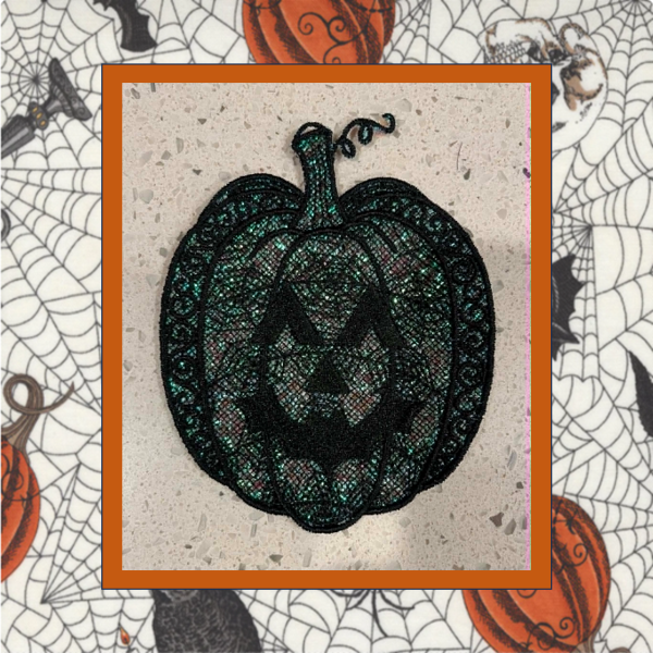 Black lace jack-o'-lantern machine embroidery ornament with shimmering green Mylar, decorative scrollwork, and a curled pumpkin stem.