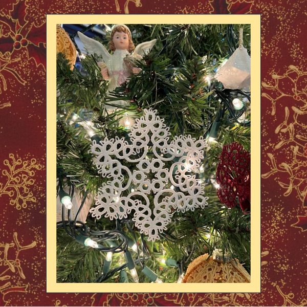 A delicate tatted free-standing lace star snowflake ornament, stitched in white thread on a Christmas tree.