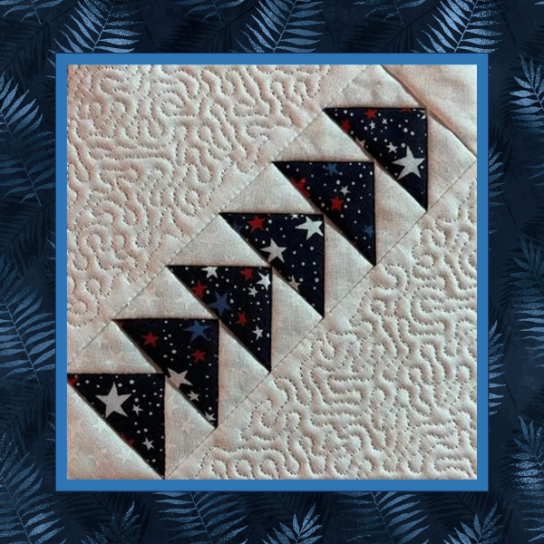 Patriotic right-facing diagonal Flying Geese quilt block stitched in the hoop with star-print fabric and coordinating stippled quilt block shown on light fabric background.