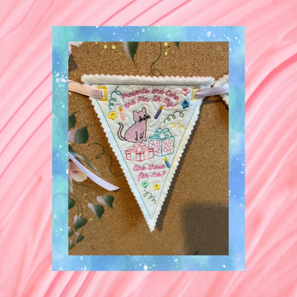 Reusable Happy Birthday bunting, pennant two of three, machine embroidery design stitched in the hoop on felt, featuring a cat, gifts, pastel stitching and pinked edges.