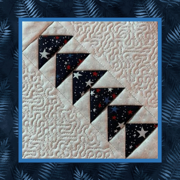 Patriotic left-facing diagonal Flying Geese quilt block stitched in the hoop with star-print fabric and coordinating stippled quilt block shown on light fabric background.