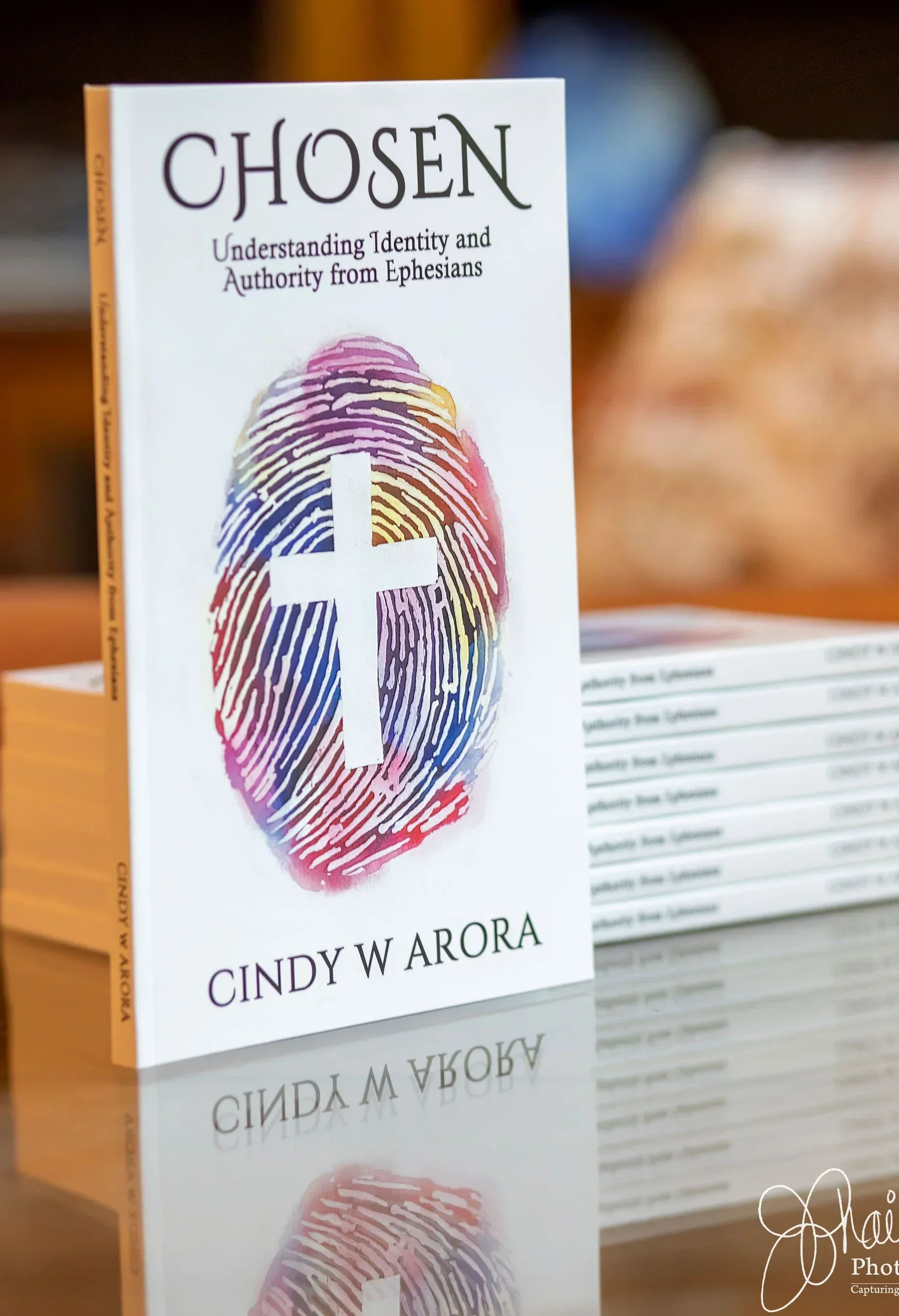 Stacked copies of the book Chosen by Cindy W Arora, featuring a cross on a colorful fingerprint on the cover.