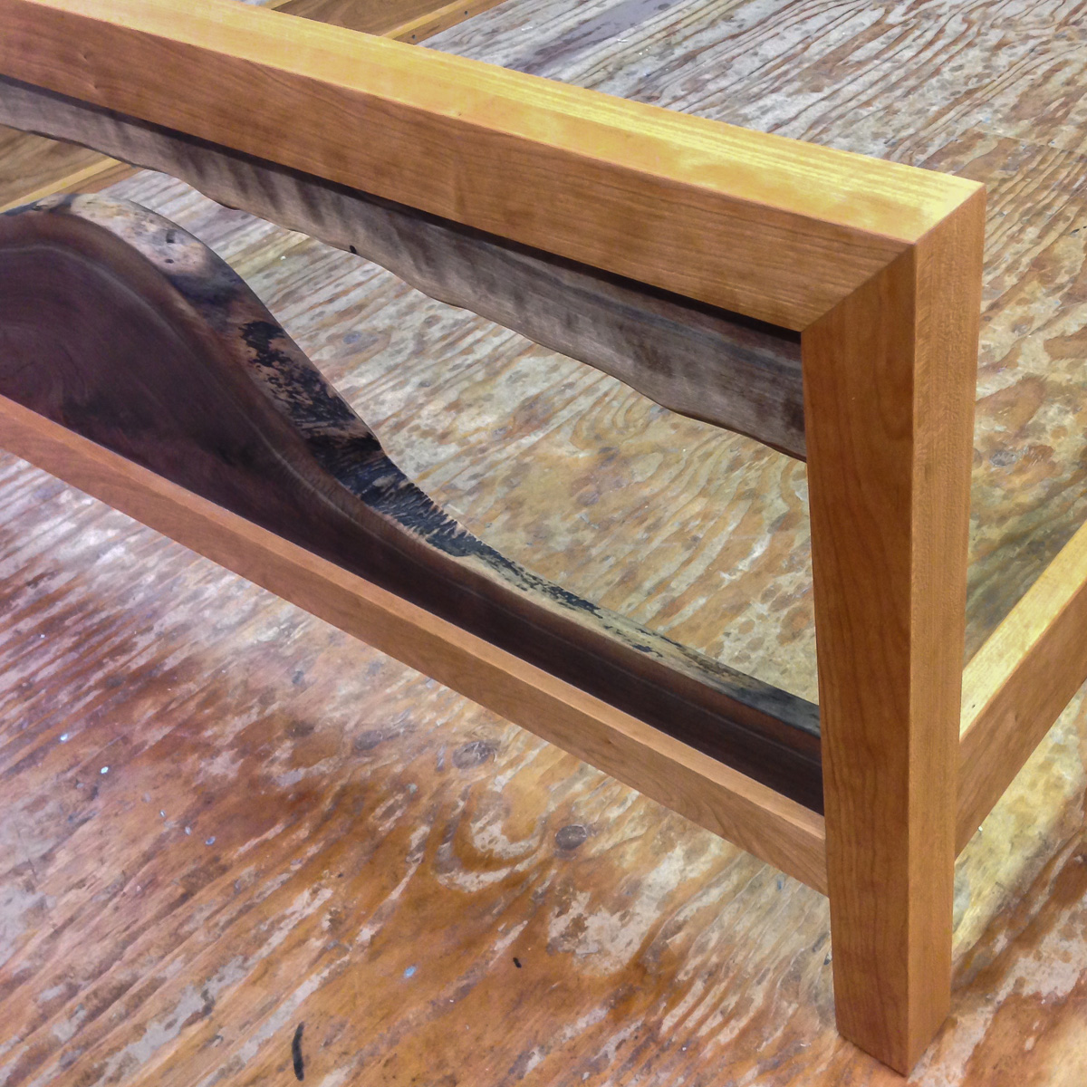 Detail of a footboard with live edge walnut elements in a cherry mitered frame