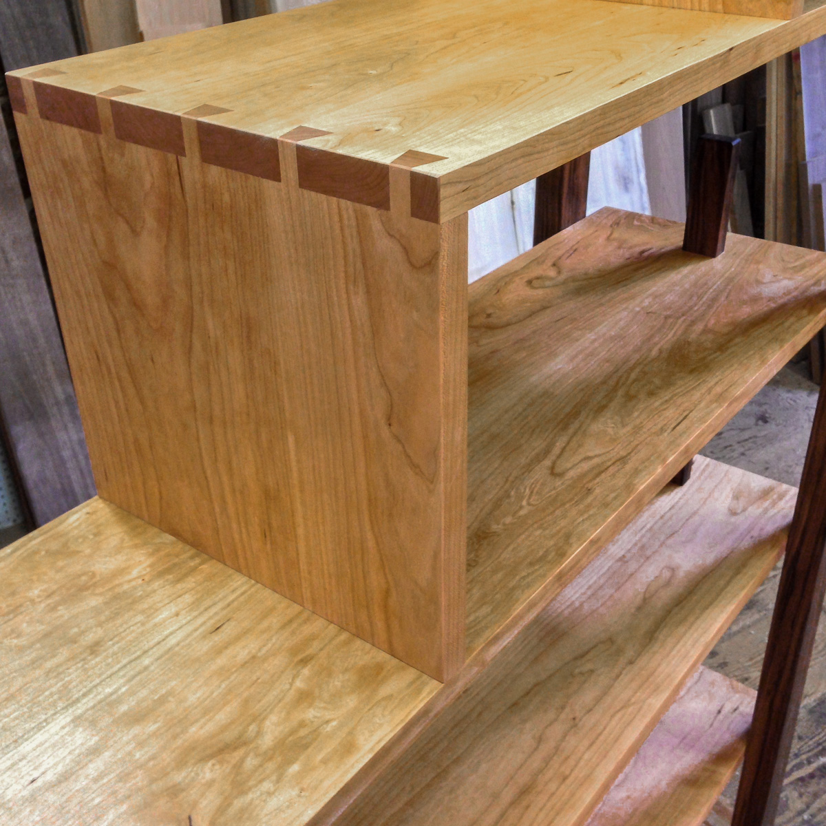 Detail of a stepped cherry shelving unit with dovetail corners, walnut legs and bookends.