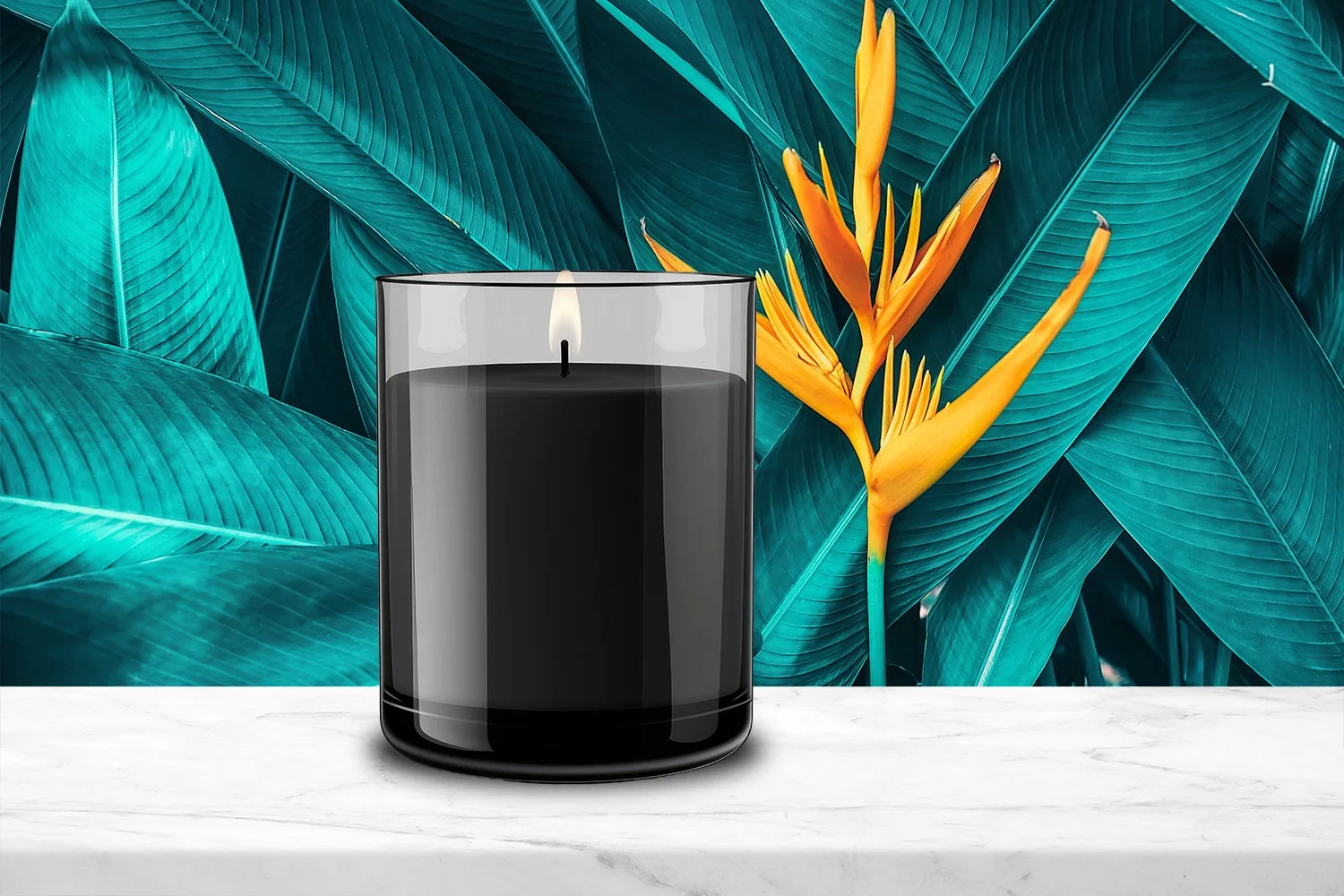 A black candle with a lit flame sitting on a white marble surface, with large teal leaves and a yellow-orange tropical flower in the background.