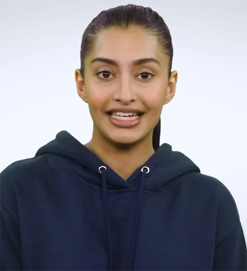 Young woman with brown hair tied back, wearing a navy blue hoodie, smiling slightly, facing the camera, white background.