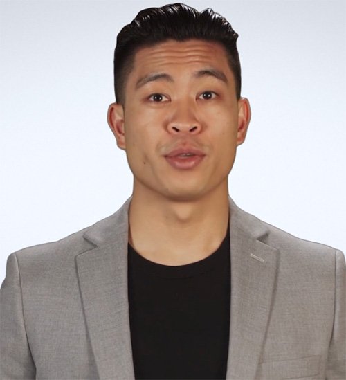 A man with short, dark hair wearing a light gray blazer and a black shirt, speaking or presenting against a plain white background.